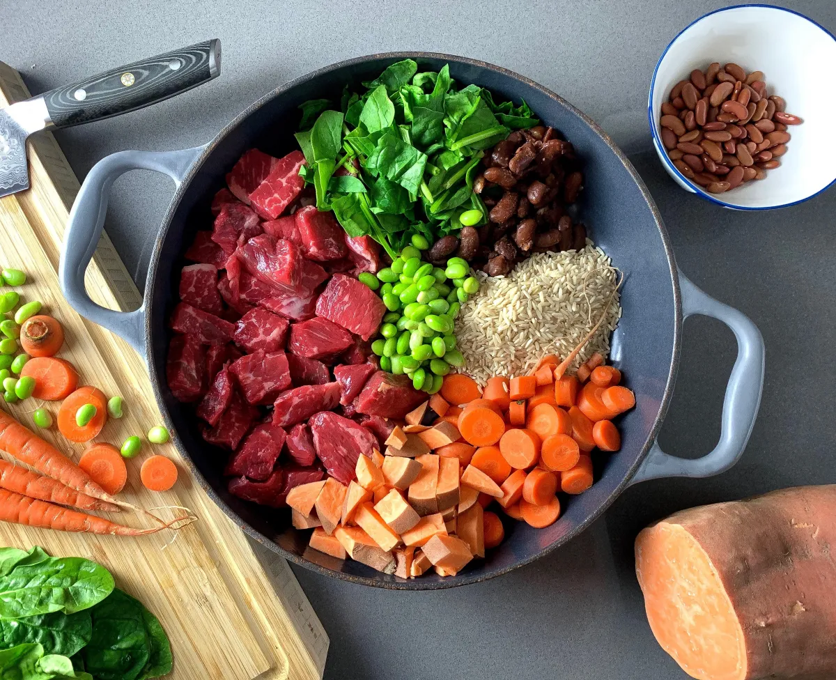 A spoon scooping chunky beef and vegetable gravy from a white bowl on a bright kitchen counter, warm natural light