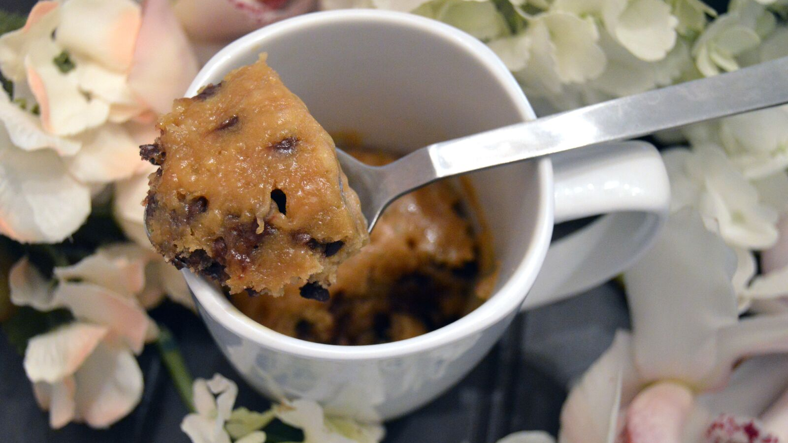 A spoon scooping into a warm chocolate chip mug cookie with a soft center