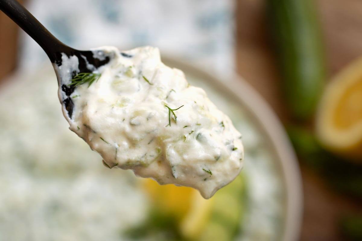 A spoon scooping thick tzatziki from a bowl showing its creamy texture with grated cucumber and herbs