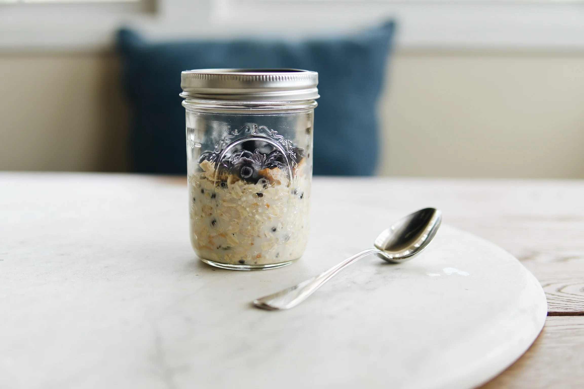 A spoon stirring a bowl of overnight muesli with oats, yogurt, chia seeds, and berries on a kitchen counter