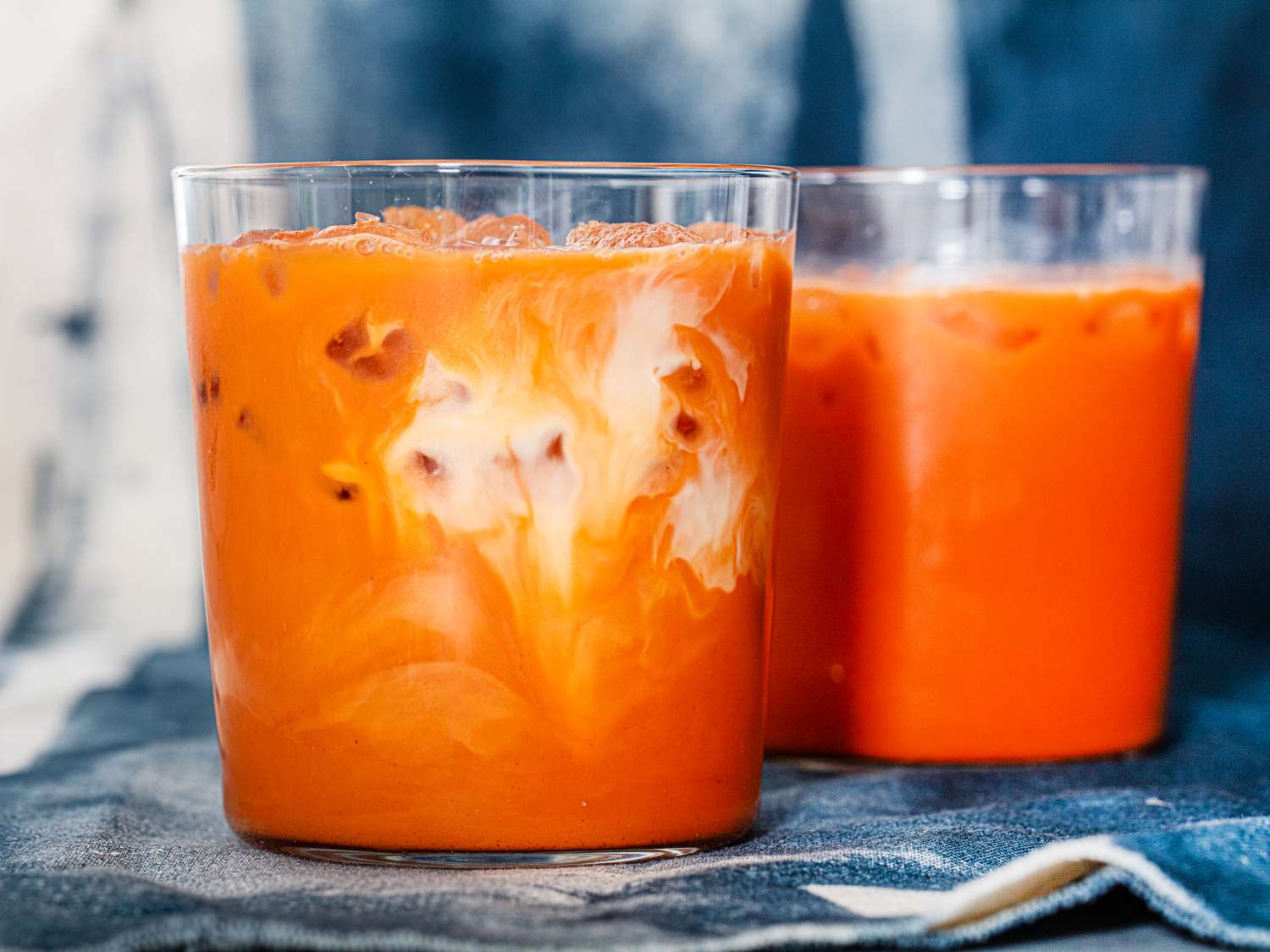 A spoon stirring a glass of Thai iced tea as creamy milk swirls into the amber tea over ice