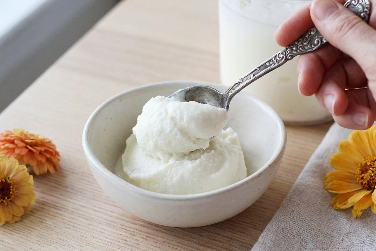 A spoonful of vanilla bean ice cream being served into a small ceramic bowl on a simple table setting