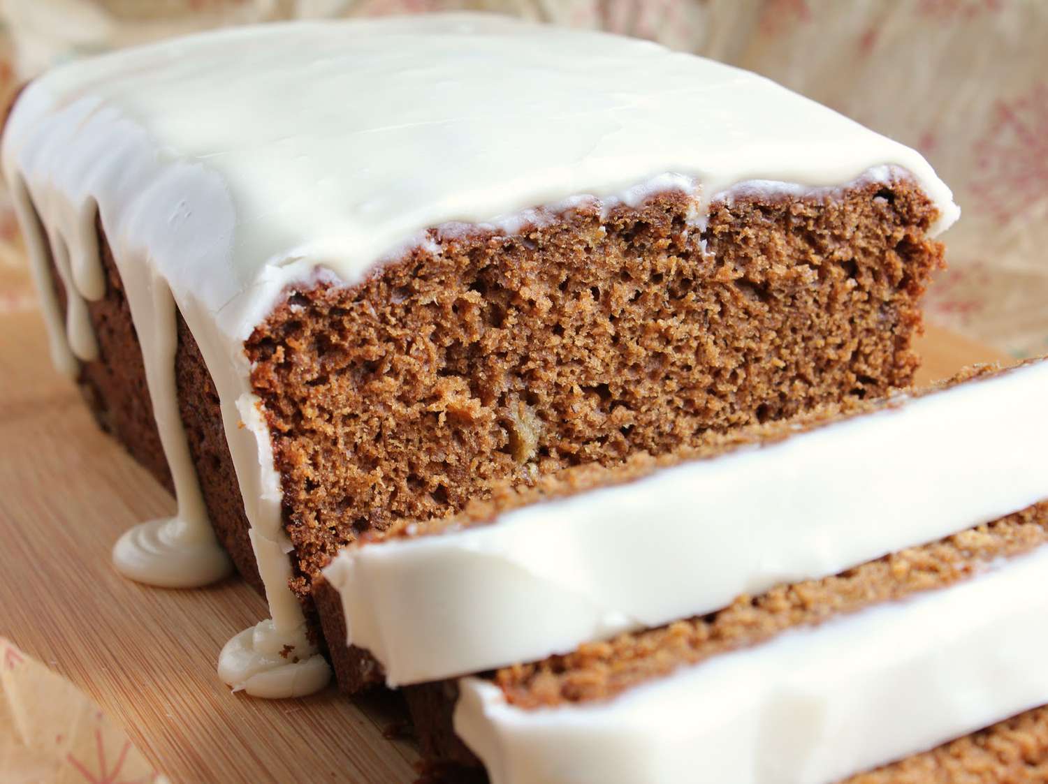 A square of moist gingerbread cake topped with a thin vanilla glaze on a small plate, with a fork beside it on a warm wood table