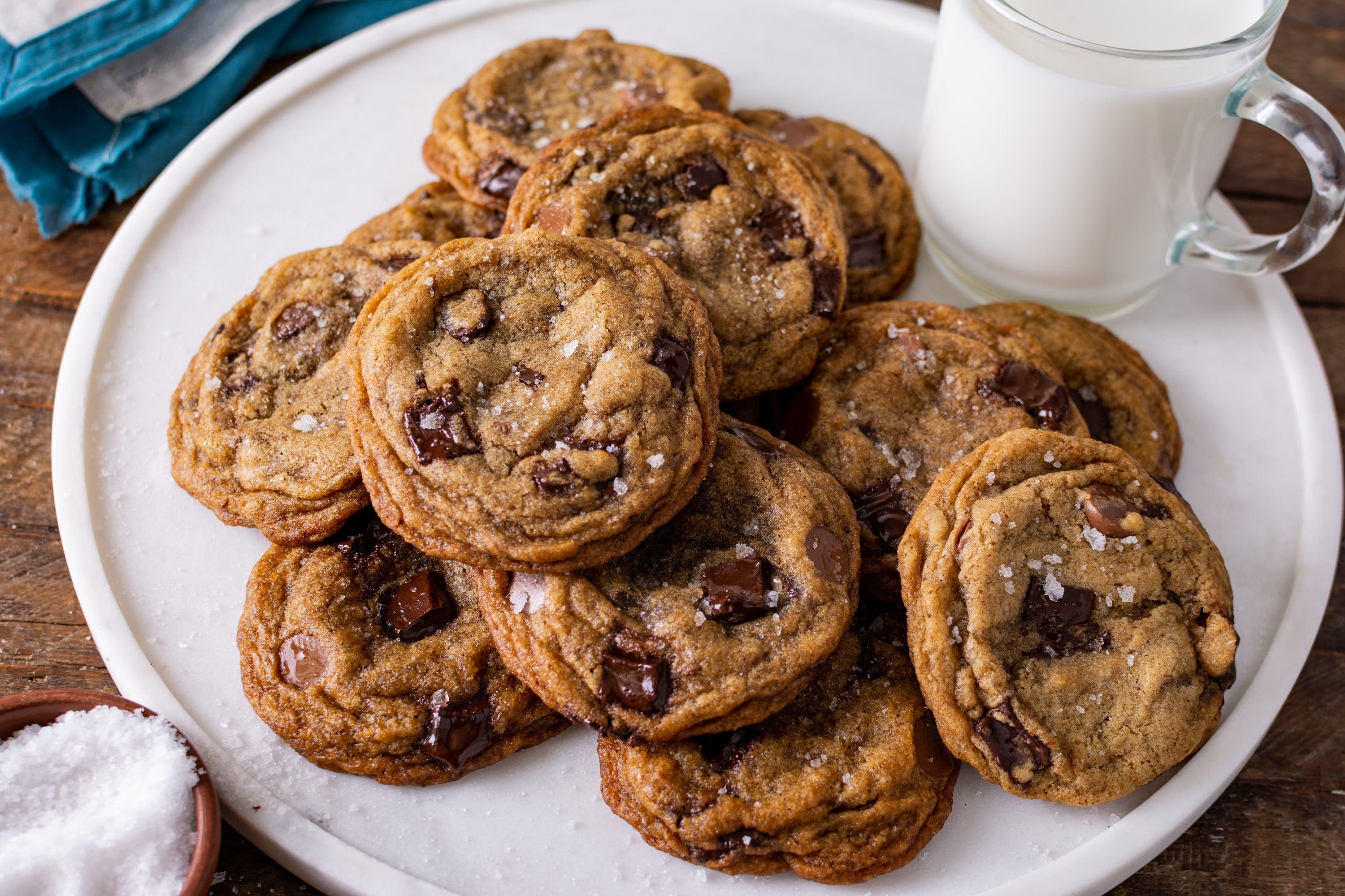 A stack of brown butter chocolate chip cookies with crisp golden edges and melty chocolate chunks on a wooden board in a bright home kitchen