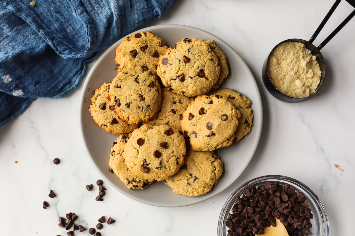 A stack of chewy gluten-free chocolate chip cookies with crisp golden edges and melty chocolate chips on a white plate on a warm kitchen table