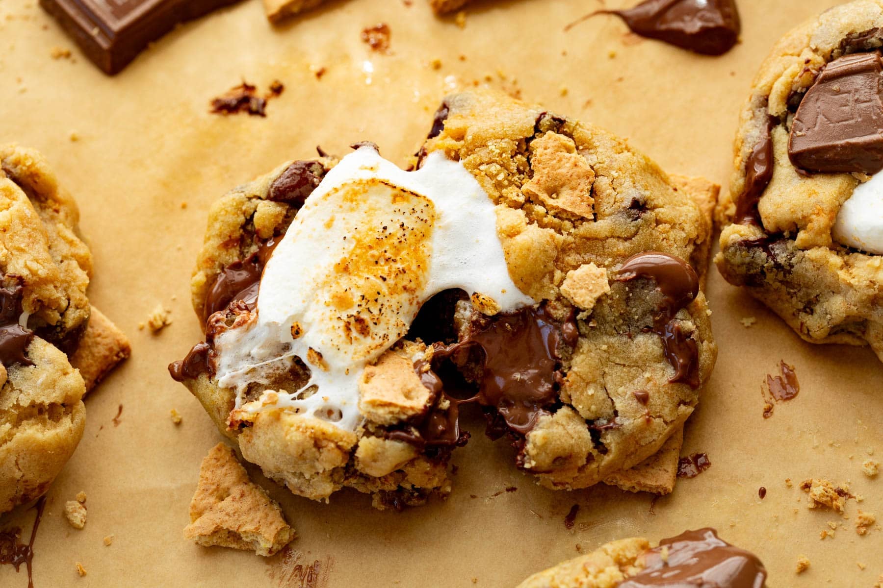 A stack of freshly baked s’mores cookies with toasted marshmallow pieces and melted chocolate chunks cooling on a wire rack on a warm-toned kitchen counter