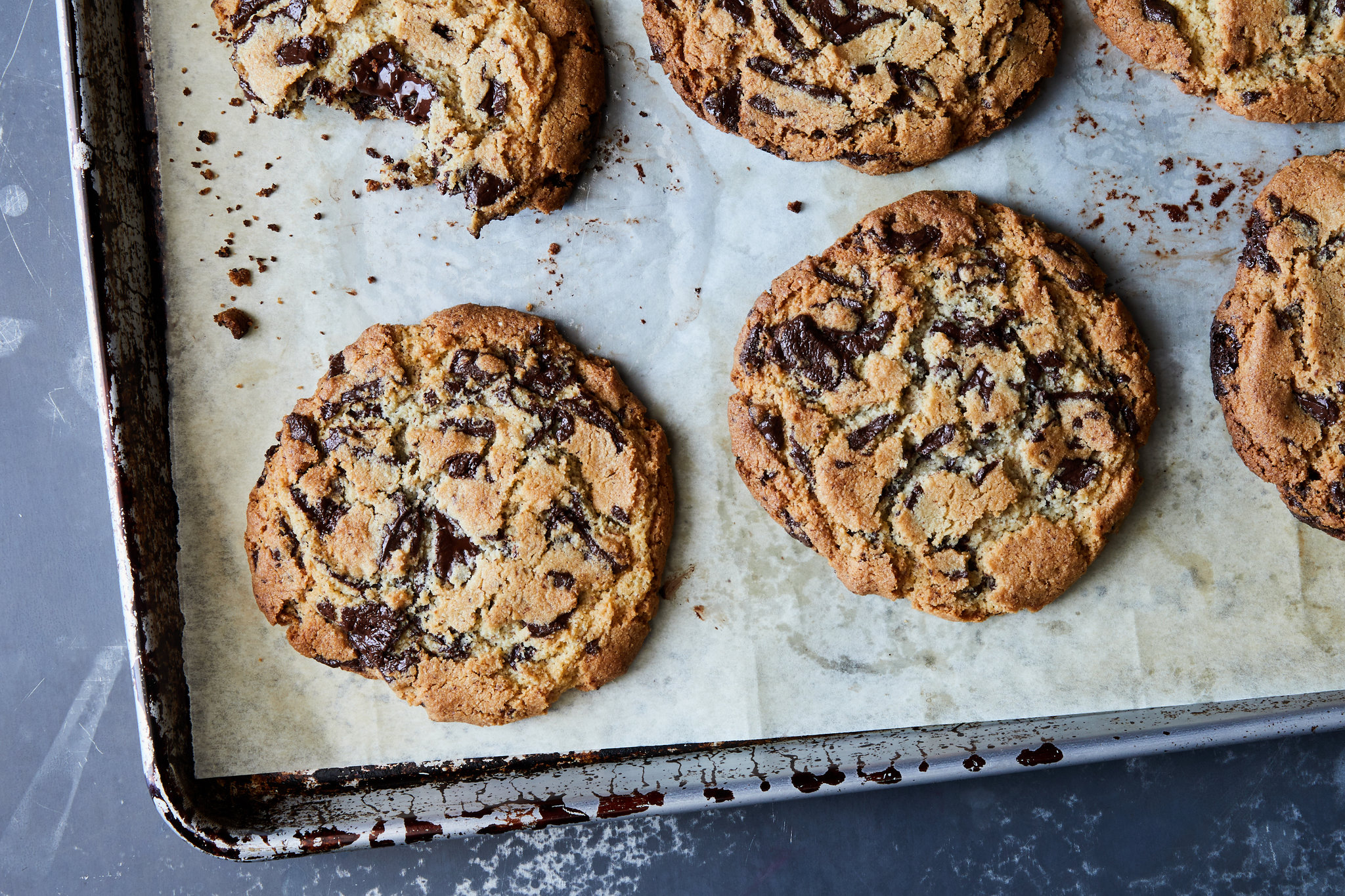 A stack of gluten free chocolate chip cookies with crisp edges and melty chocolate chips on a parchment lined plate on a warm kitchen table