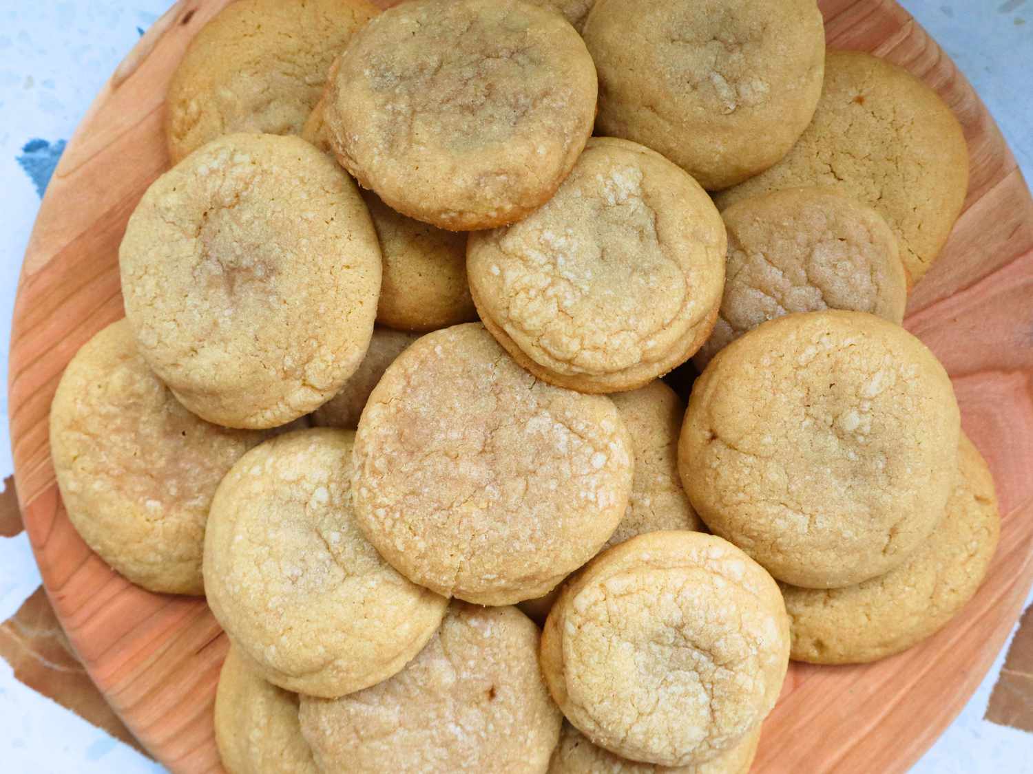 A stack of golden brown chipless cookies with slightly crisp edges and soft centers on a white plate on a warm-toned kitchen table