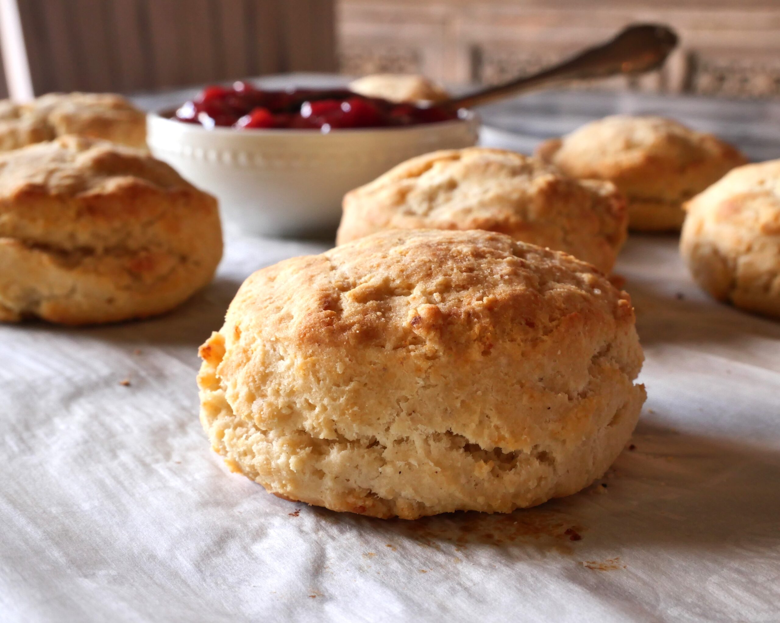 A stack of golden brown gluten free biscuits on a white plate with a pat of butter melting on top, set on a warm kitchen table with soft natural light