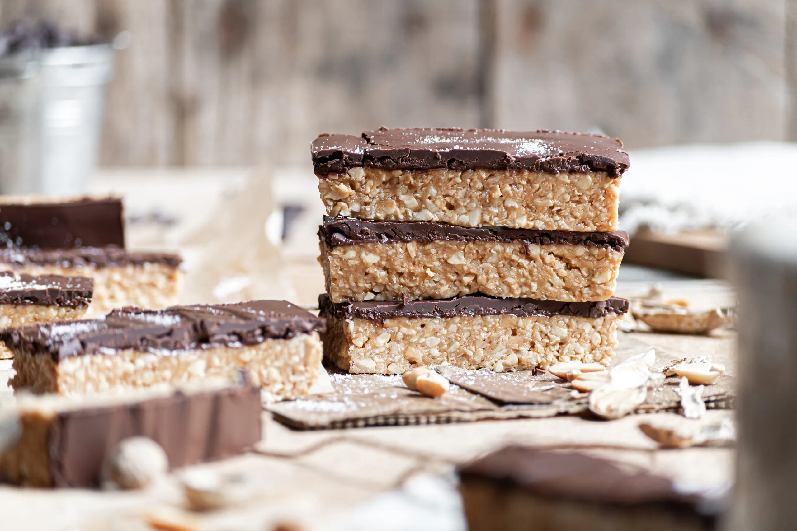 A stack of homemade no-bake peanut butter protein bars with a glossy chocolate drizzle on a parchment-lined wooden board on a bright kitchen counter