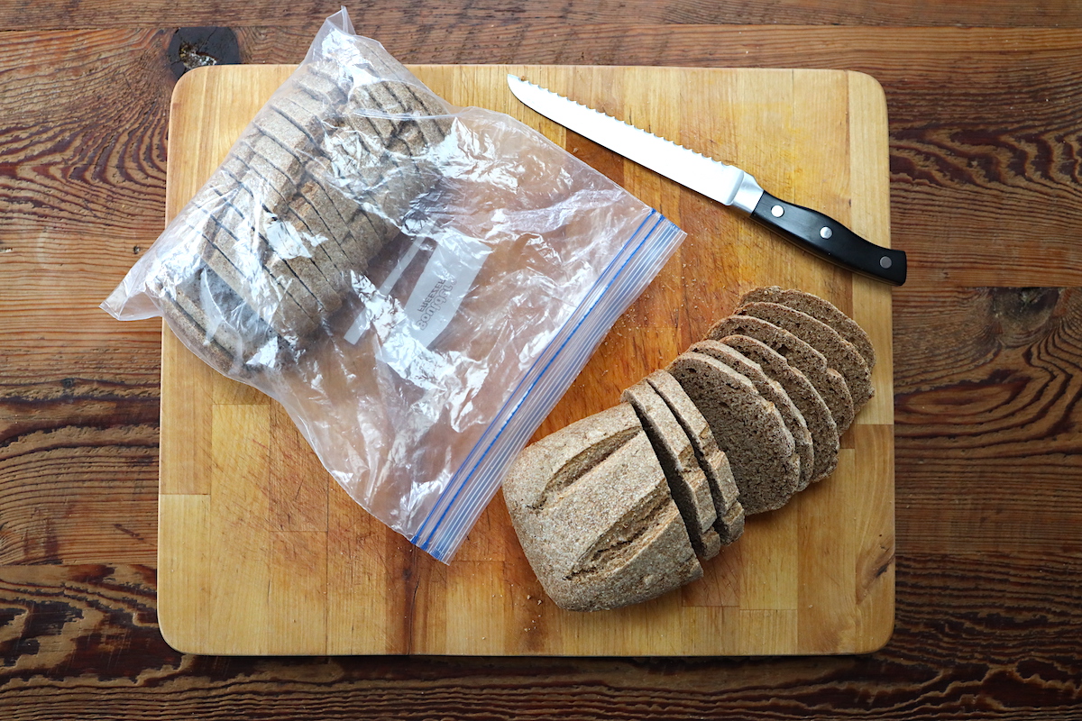 A stack of sliced whole grain sourdough bread on parchment paper beside an open freezer-safe bag on a kitchen counter