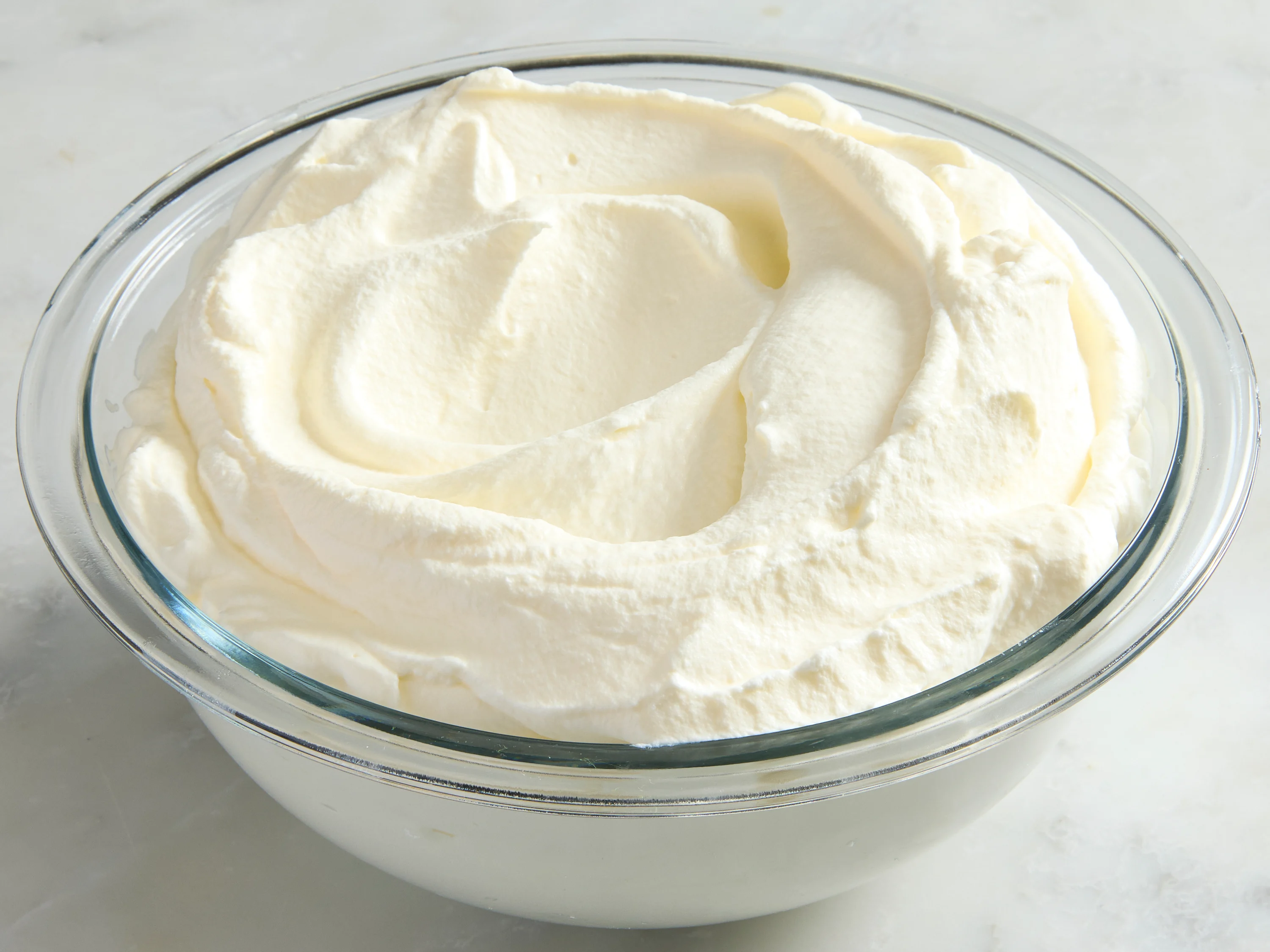A stainless mixing bowl of whipped cream at stiff peaks with a handheld mixer lifted above the bowl