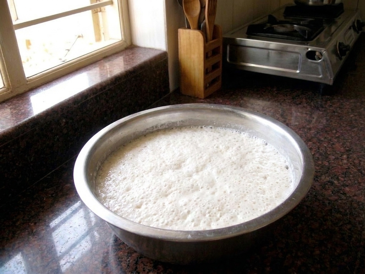 A stainless steel bowl filled with airy, fermented idli batter with small bubbles on the surface on a kitchen counter
