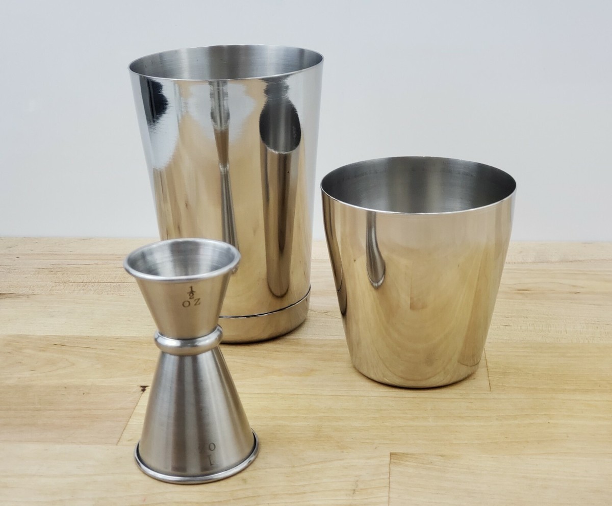 A stainless steel cocktail shaker on a clean kitchen counter next to a jigger and citrus