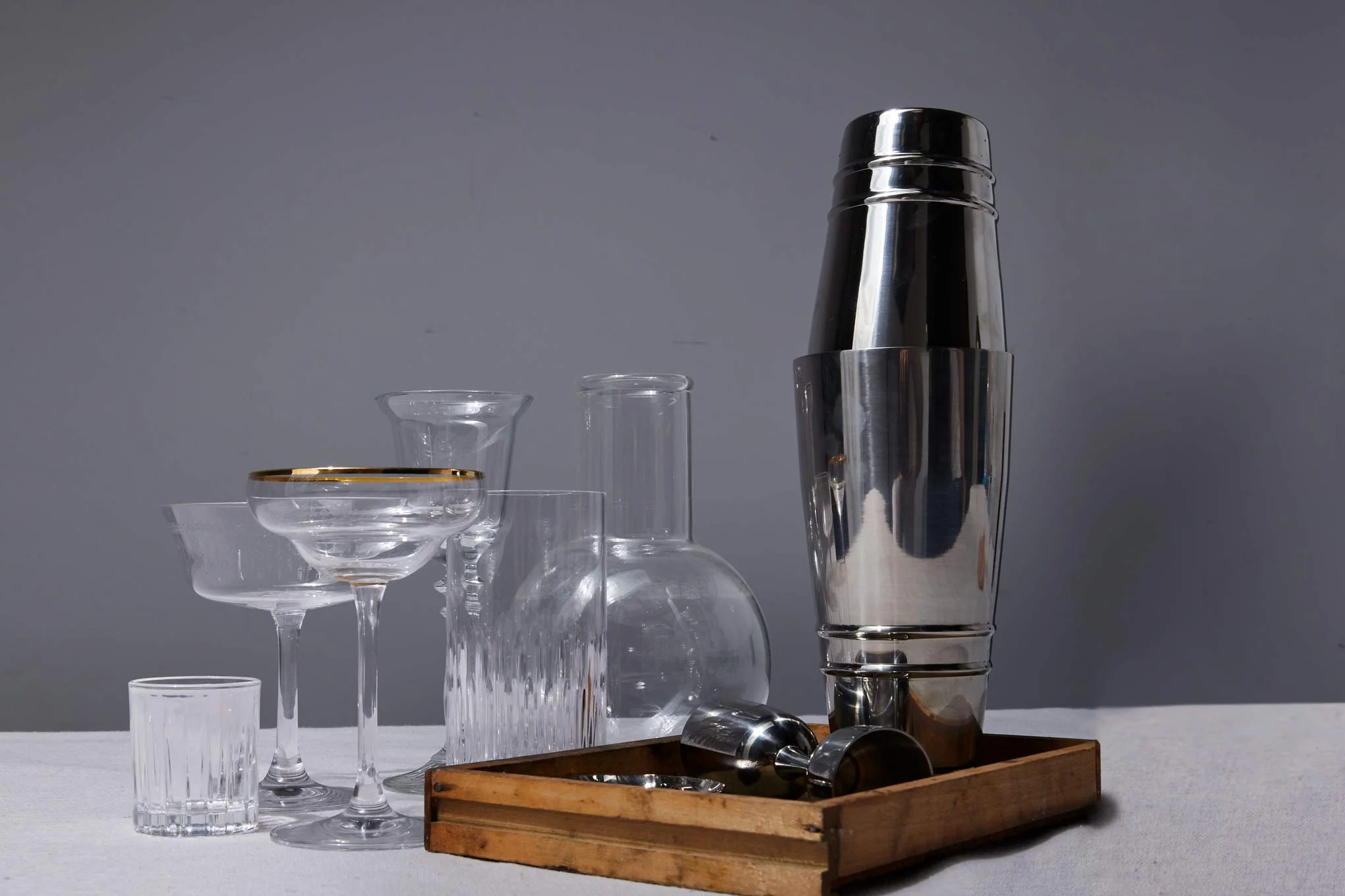 A stainless steel cocktail shaker on a kitchen counter next to neatly lined shot glasses