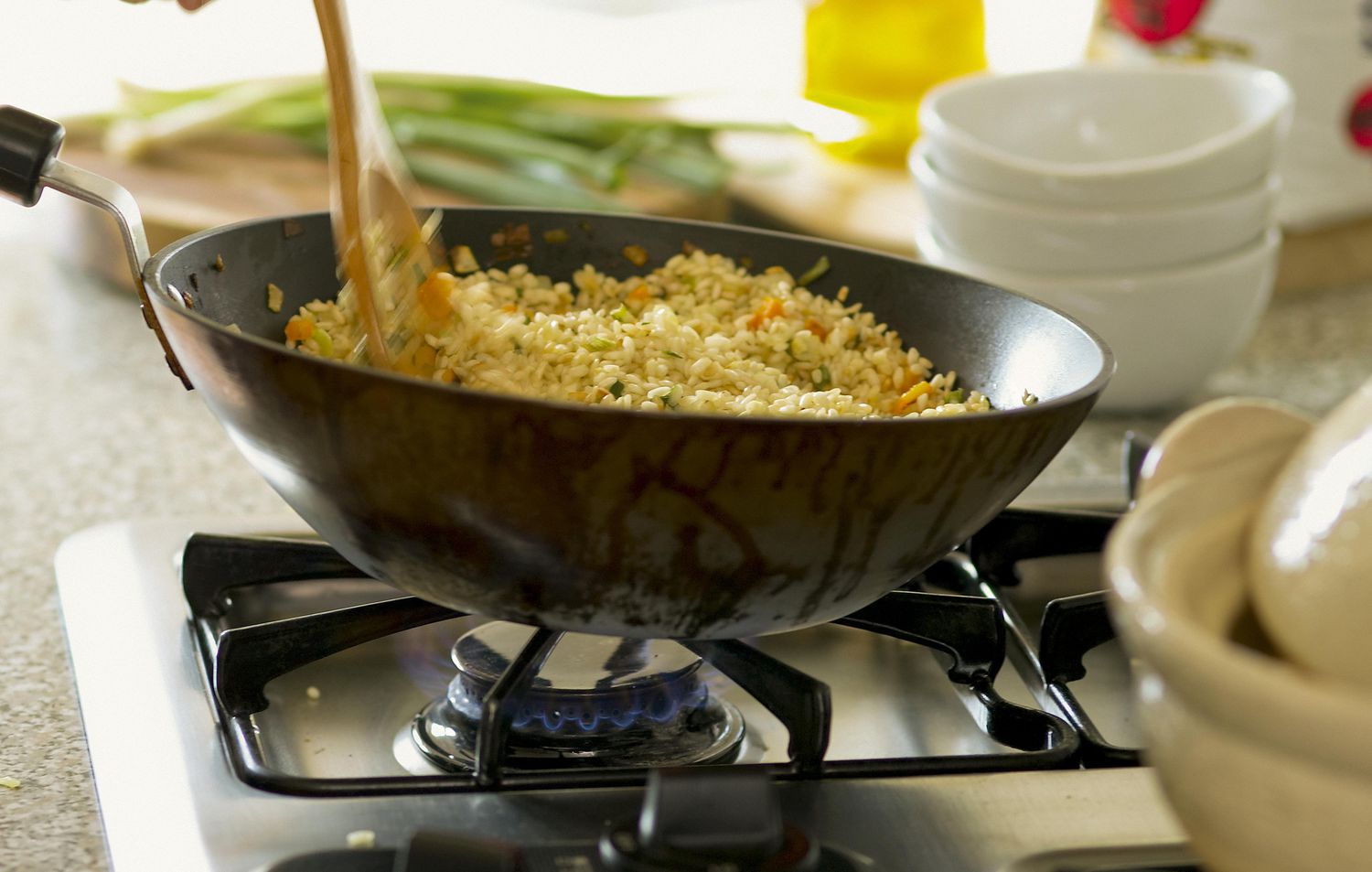 A stainless steel skillet on a stove with rice being stirred, showing browned crispy bits forming, with a spatula mid-motion