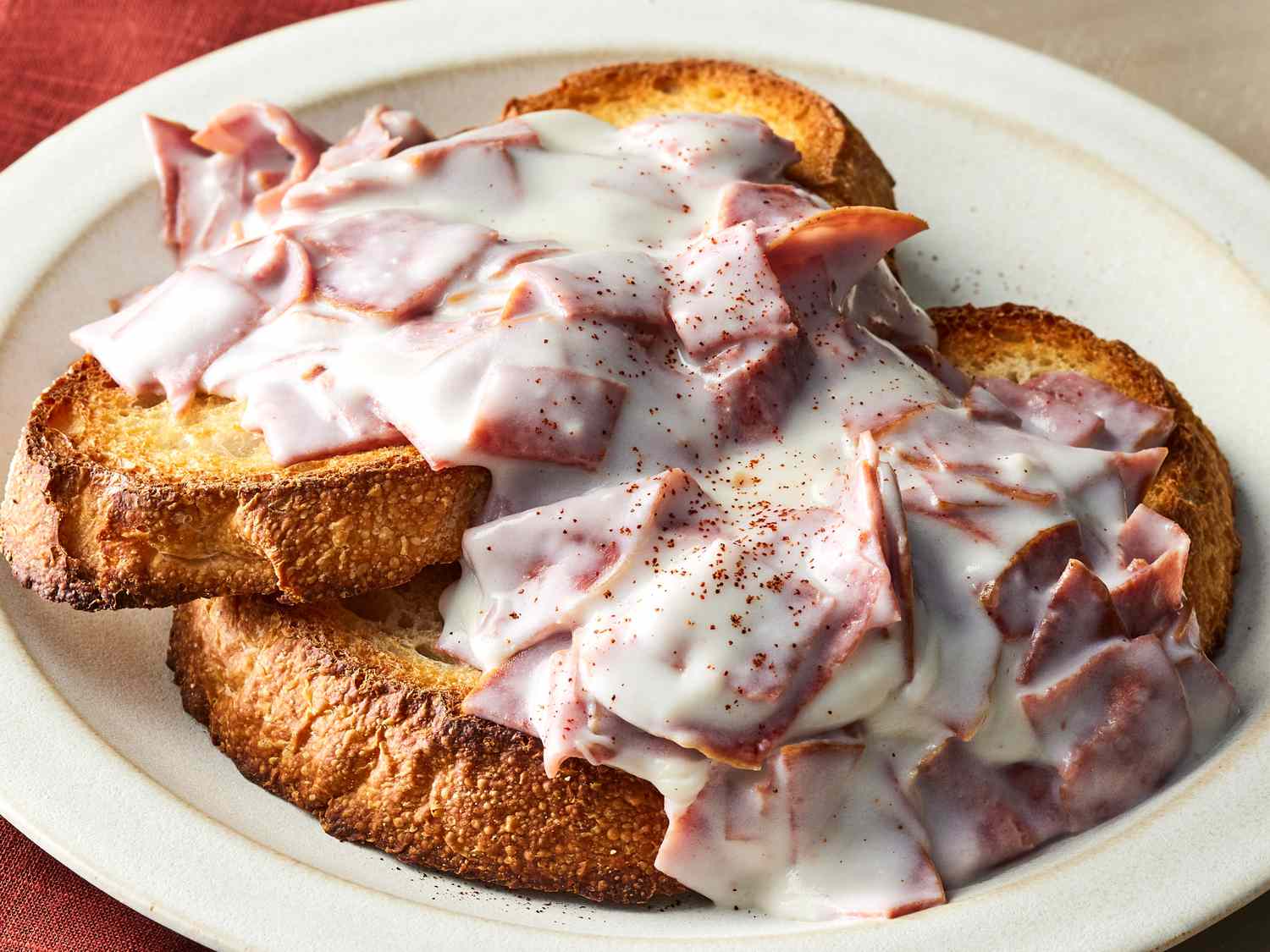 A stainless steel skillet on a stovetop with creamed chipped beef sauce being stirred with a wooden spoon, steam rising