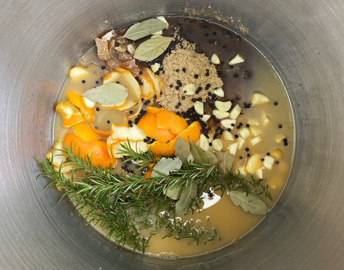 A stainless steel stockpot of turkey brine with floating bay leaves, citrus halves, and herbs on a stovetop