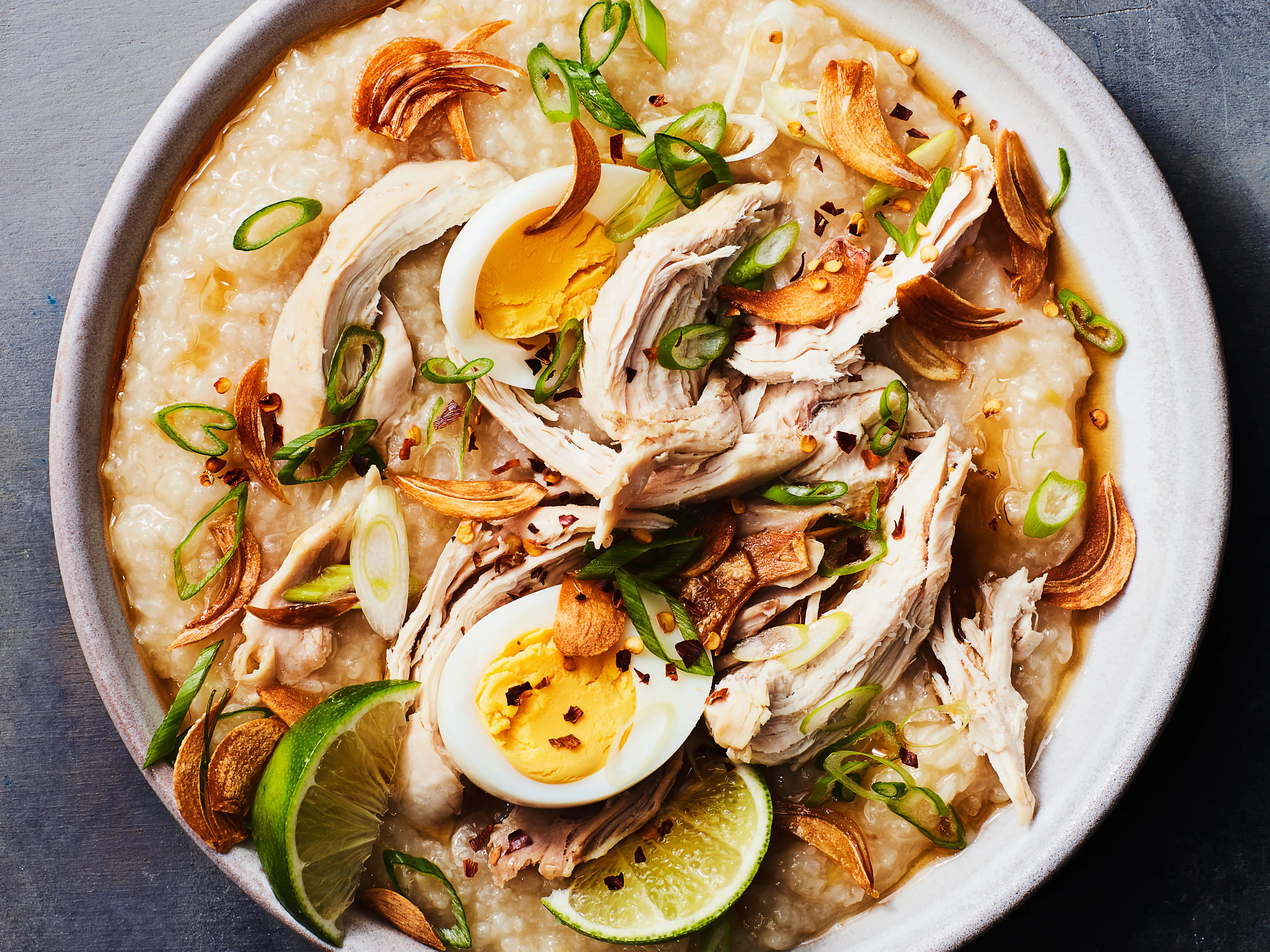 A steaming bowl of Filipino arroz caldo (lugaw) topped with sliced scallions, crispy fried garlic, and a wedge of calamansi on a warm kitchen table