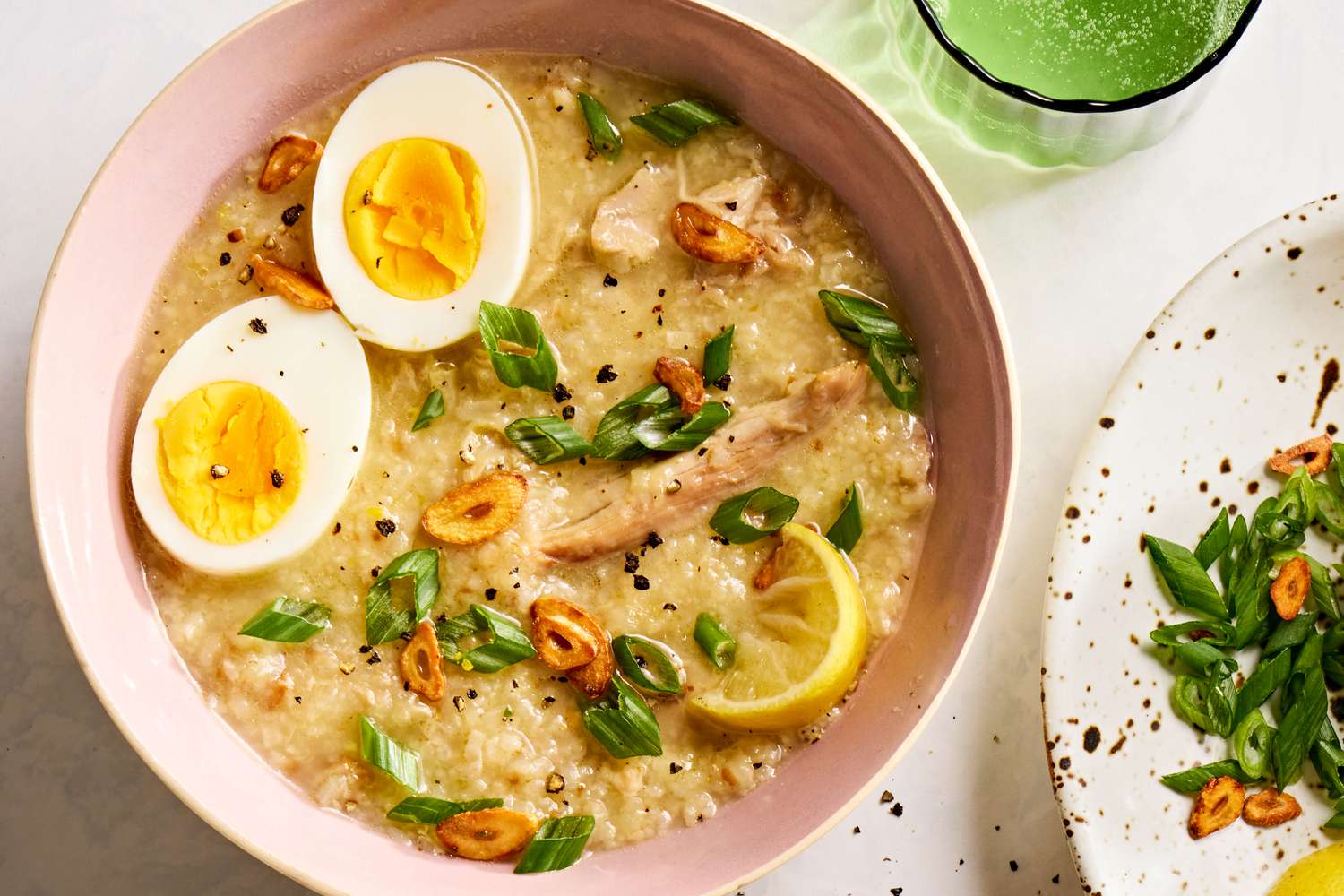 A steaming bowl of Filipino arroz caldo topped with sliced scallions, crispy garlic, and a wedge of calamansi on a rustic wooden table