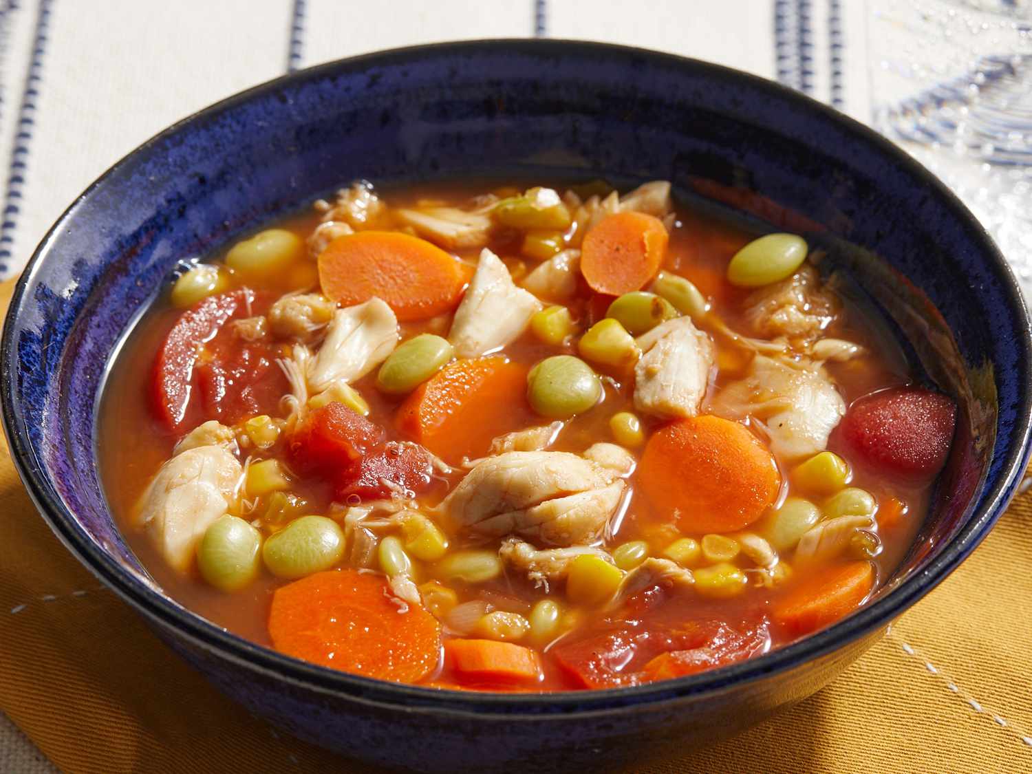 A steaming bowl of Maryland crab soup filled with vegetables and lump crab on a rustic kitchen table with a spoon and saltines