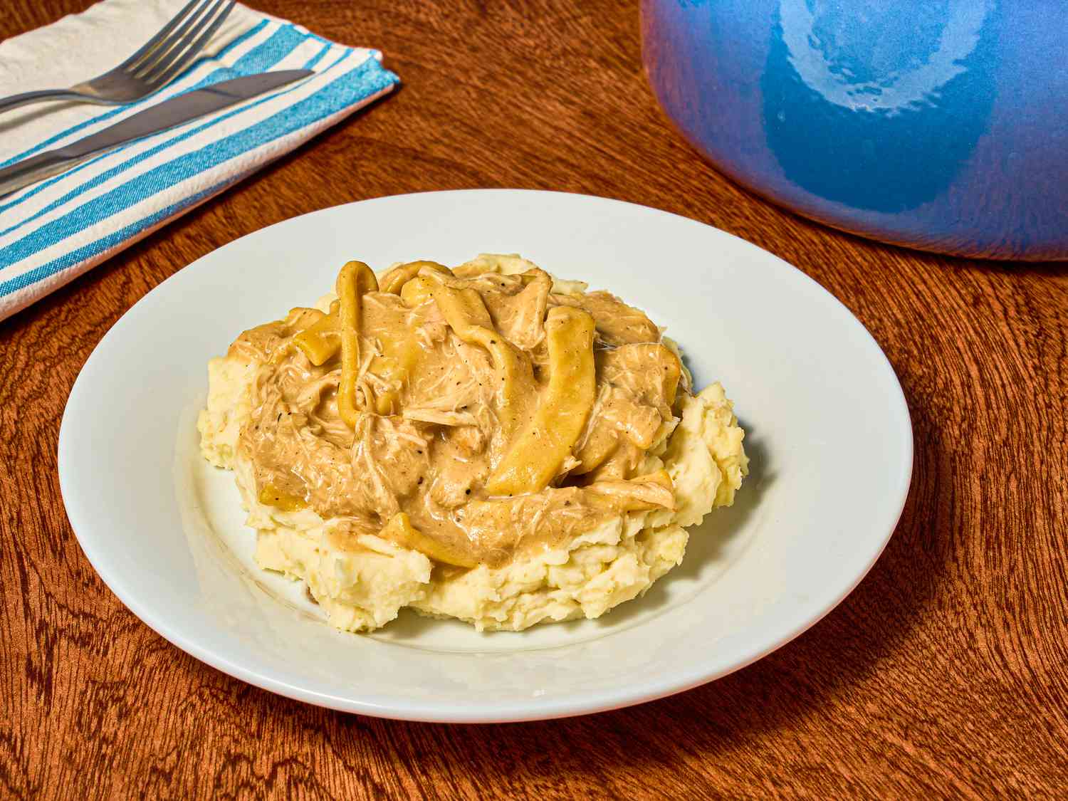 A steaming bowl of chicken and noodles made with egg noodles in a creamy broth, garnished with parsley on a rustic wooden table