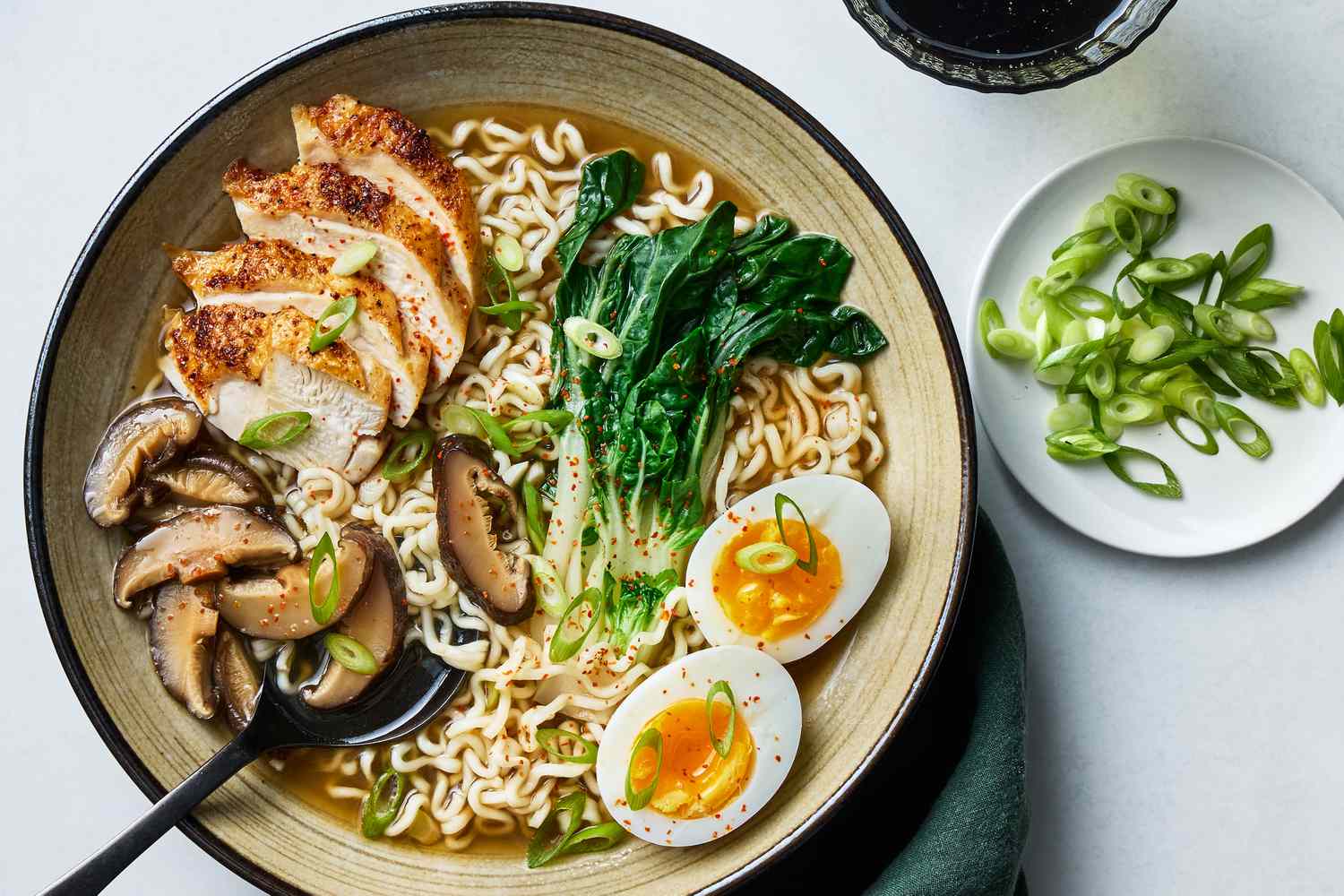 A steaming bowl of chicken ramen with springy noodles, sliced chicken, soft jammy egg, scallions, and sesame seeds on a wooden table in warm kitchen light