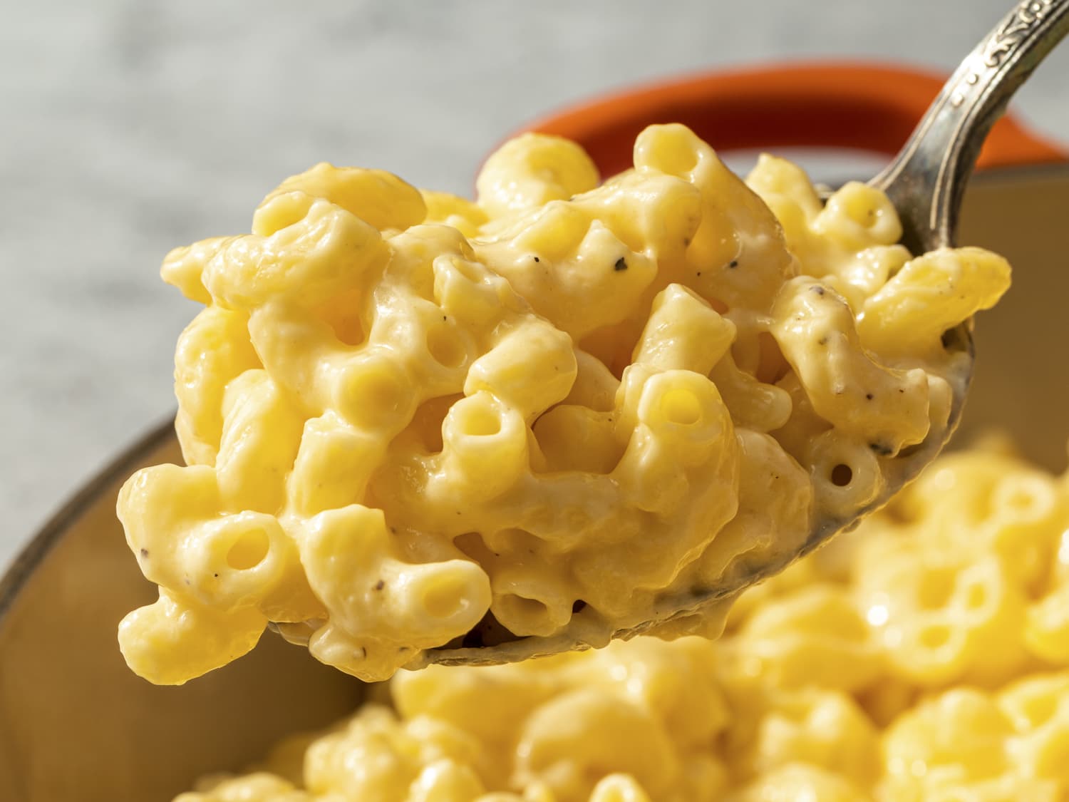 A steaming bowl of creamy gluten free mac and cheese with glossy cheddar sauce and a lightly browned crumb topping on a wooden table with a simple linen napkin