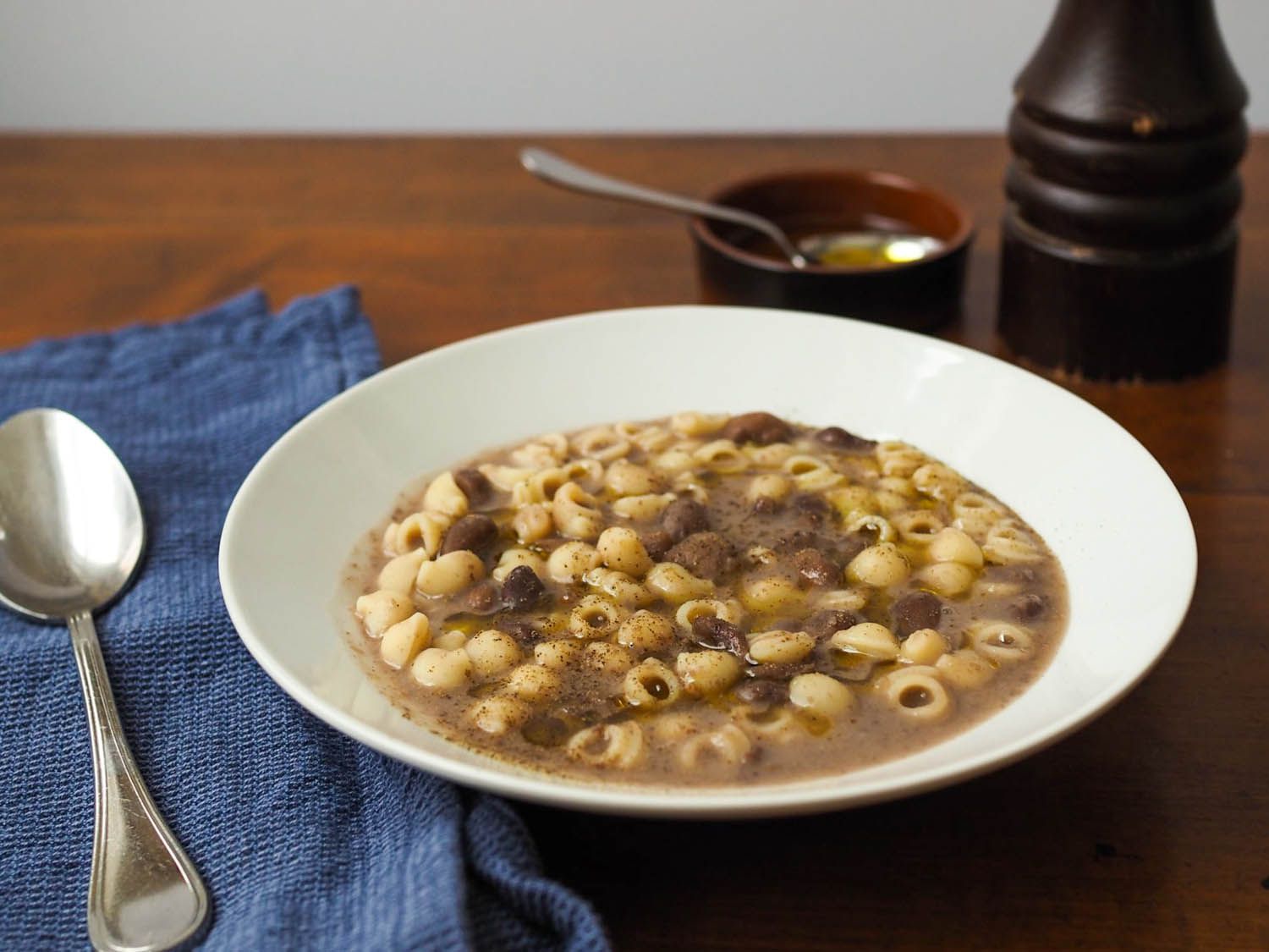 A steaming bowl of pasta e fagioli topped with grated Parmesan and a drizzle of olive oil on a wooden table, cozy dinner lighting