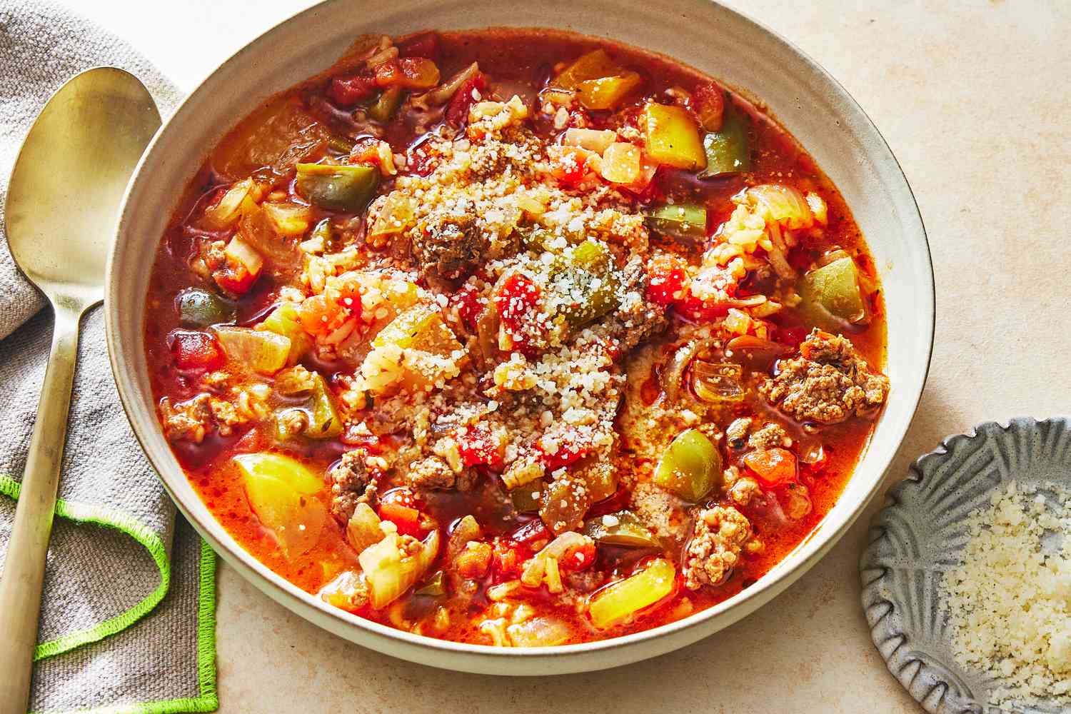 A steaming bowl of stuffed pepper soup with visible bell pepper pieces, ground beef, rice, and tomato broth, topped with chopped parsley on a rustic kitchen table