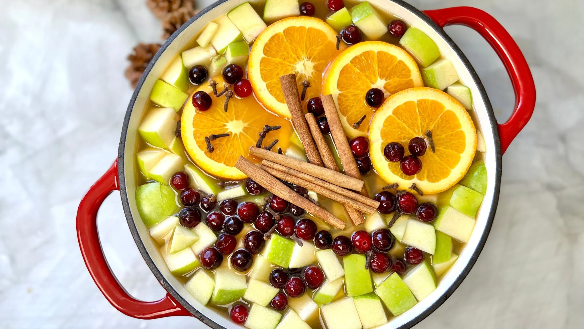 A steaming mug of mulled apple cider on a wooden table with a cinnamon stick and orange slice nearby in warm kitchen light