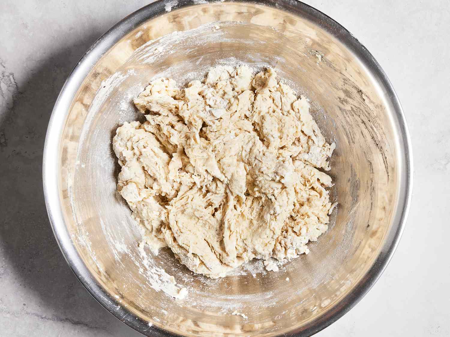 A sticky, shaggy focaccia dough being mixed in a clear bowl with a rubber spatula on a kitchen counter