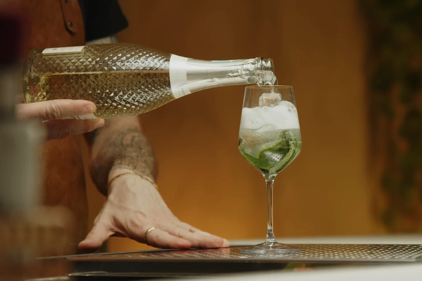A stream of Prosecco being poured into a large wine glass filled with ice cubes on a kitchen counter