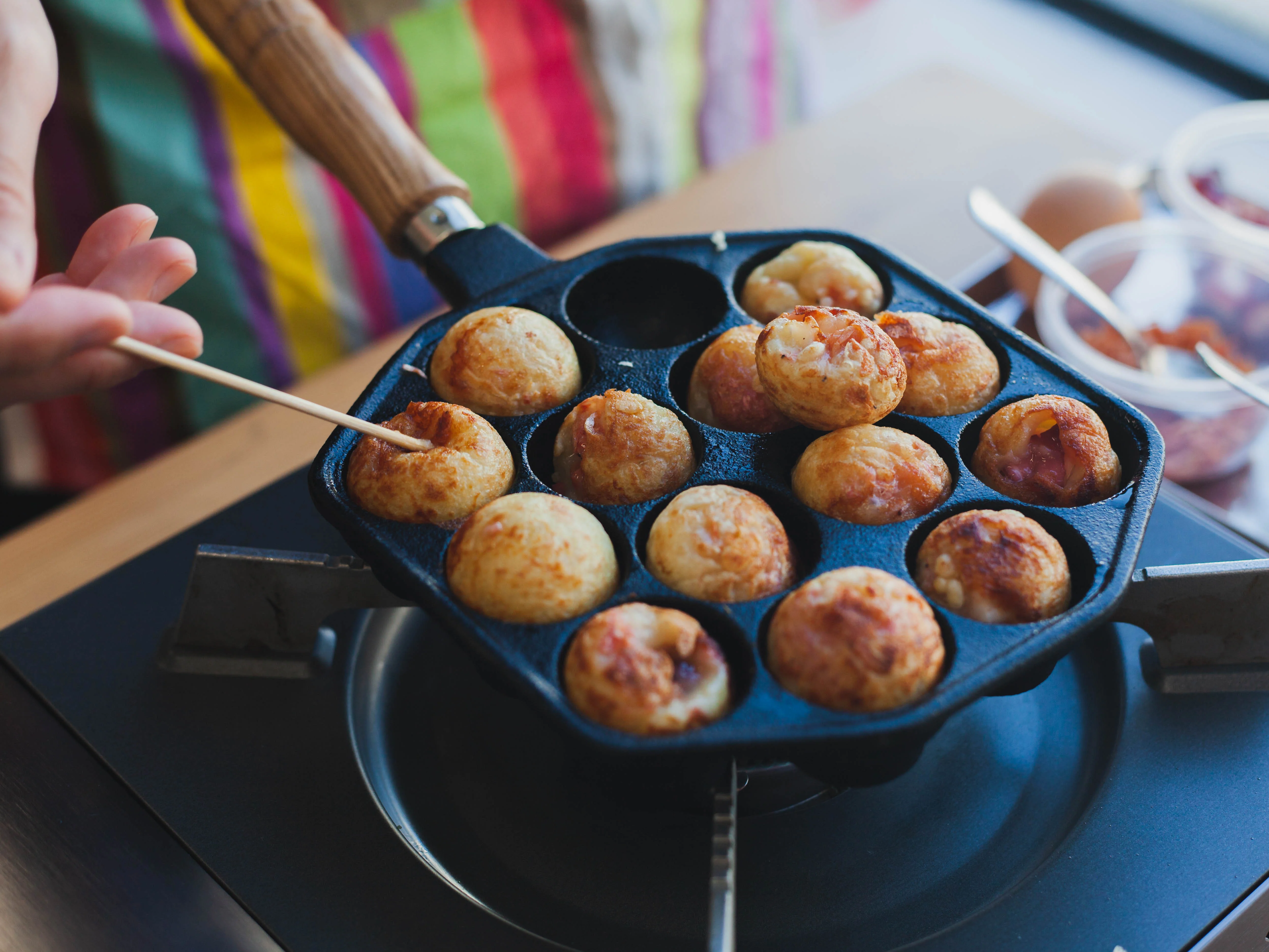 A takoyaki pan on a stovetop with each well lightly oiled and a brush resting nearby