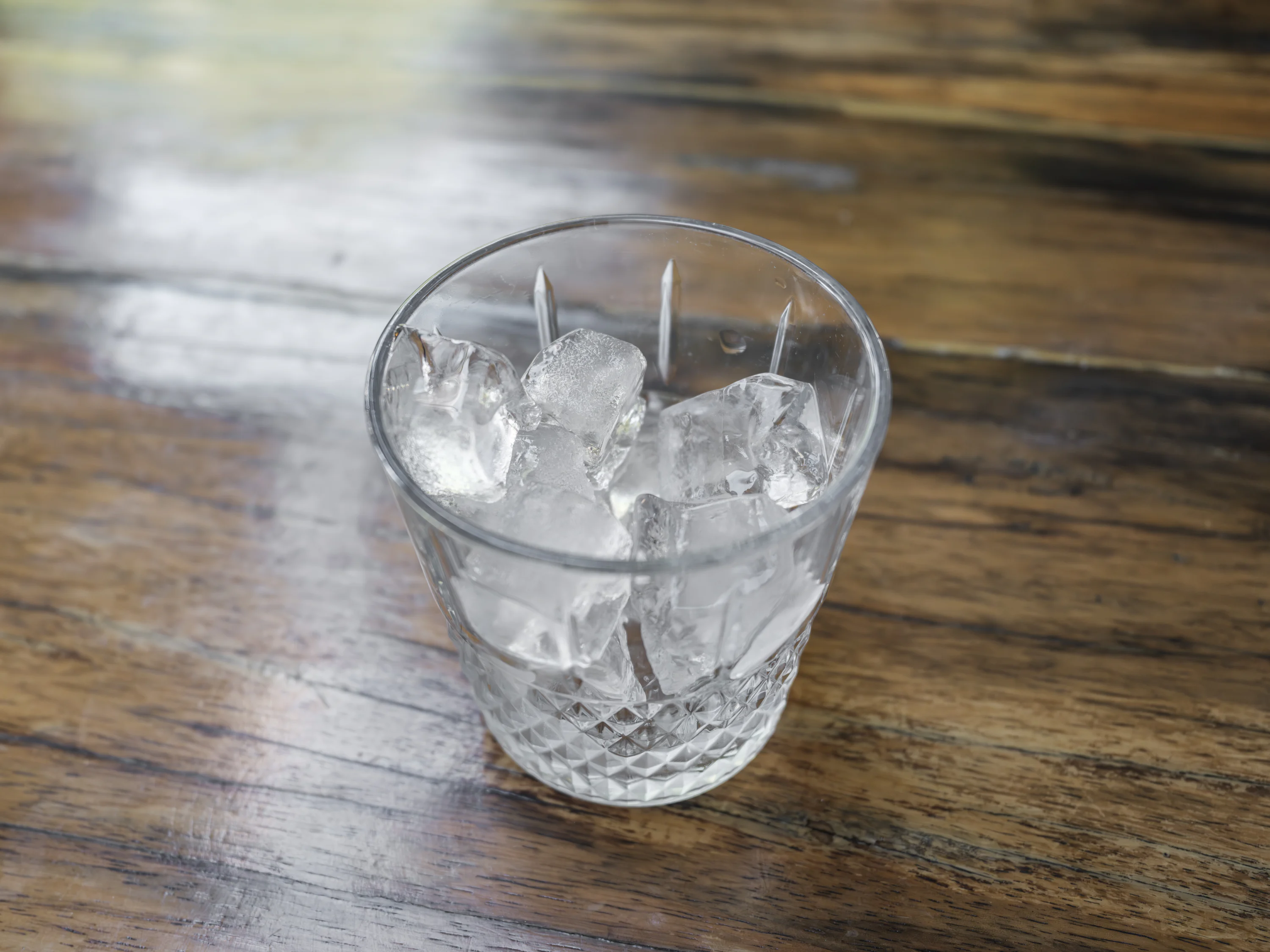 A tall clear glass packed with ice cubes on a clean kitchen counter next to a spoon