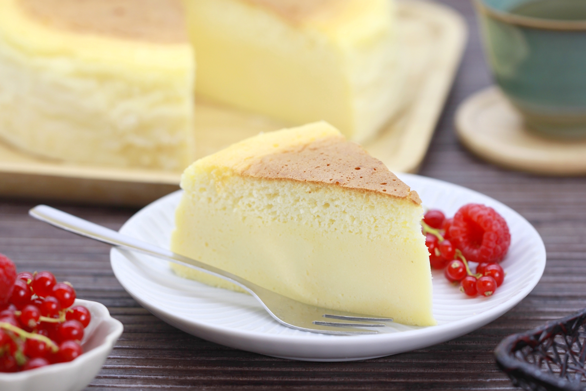 A tall, fluffy Japanese cheesecake with a lightly golden top, sliced to show its airy crumb on a simple white plate on a bright kitchen table