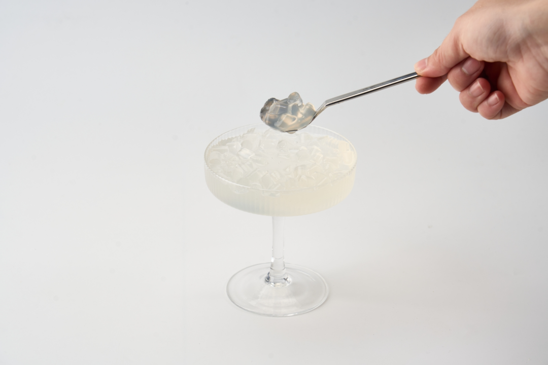 A tall glass of Japanese-style konjac jelly drink with citrus slices and spoonable jelly pieces on a light kitchen counter