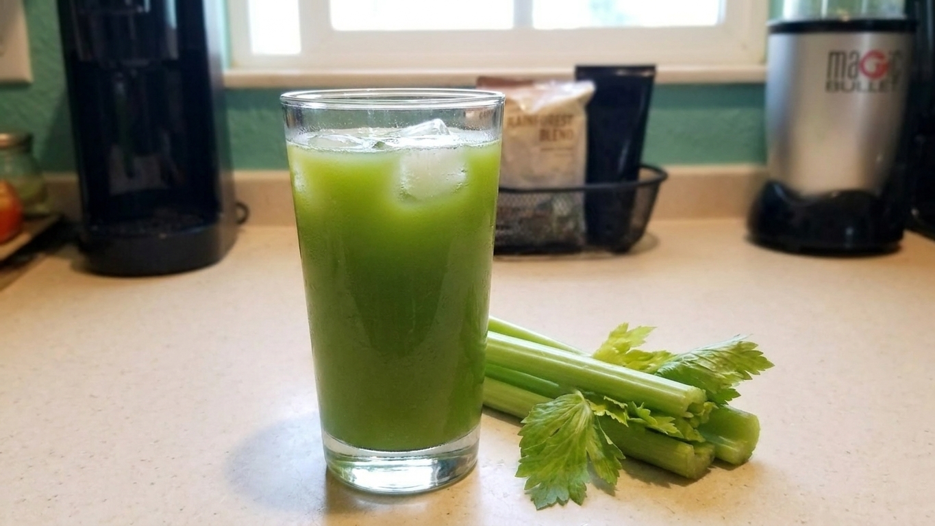A tall glass of fresh celery juice on a bright kitchen counter with a small pile of celery stalks nearby, natural morning light