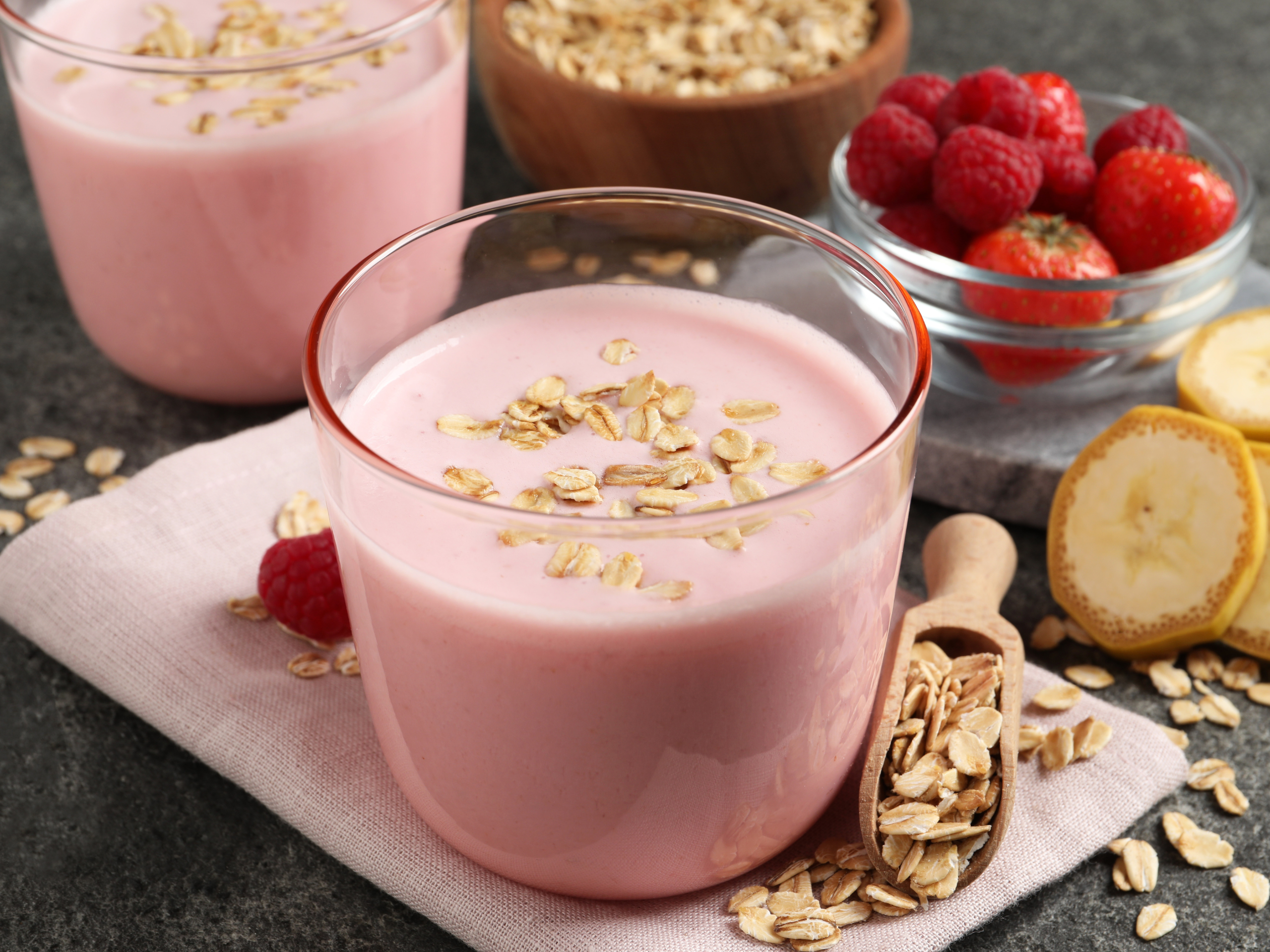 A tall glass of strawberry banana oat smoothie with a thick, creamy texture on a light kitchen counter, a few sliced strawberries nearby, natural window light
