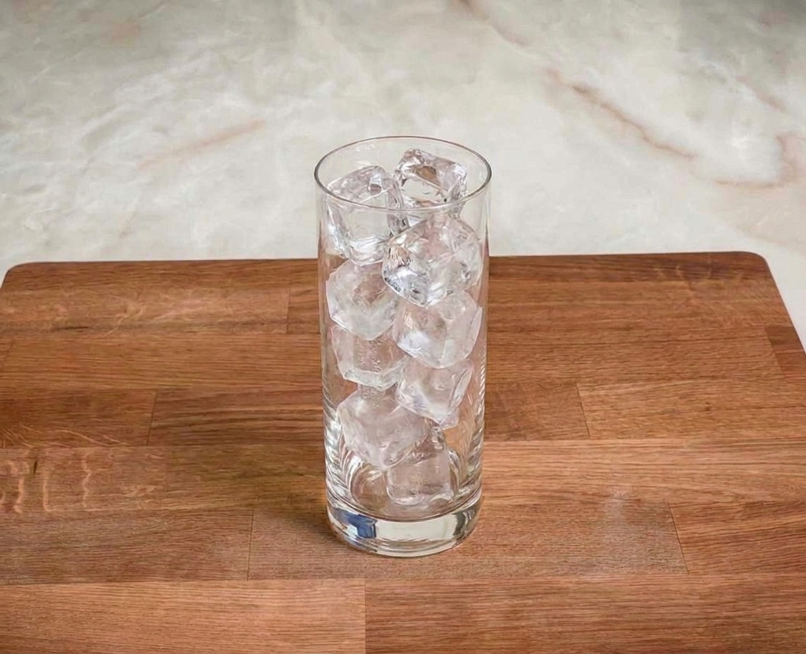 A tall highball glass filled to the top with clear ice cubes on a kitchen counter