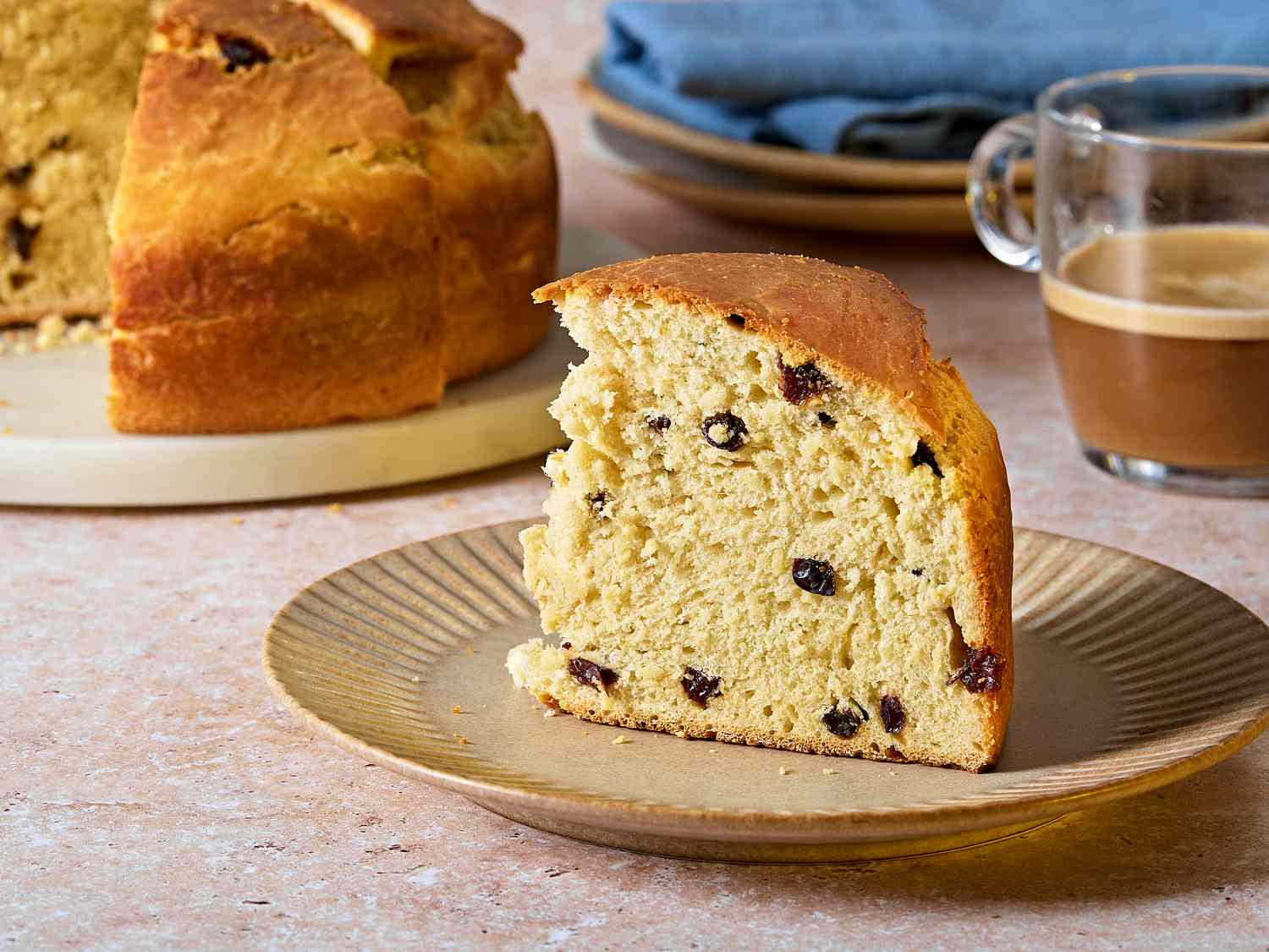 A tall homemade panettone loaf on a wooden cutting board with one slice cut, showing a fluffy, airy crumb dotted with dried fruit