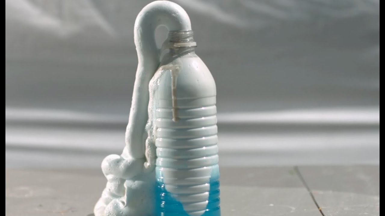 A tall stream of colorful foamy bubbles overflowing from a plastic bottle on a rimmed baking sheet on a bright kitchen counter