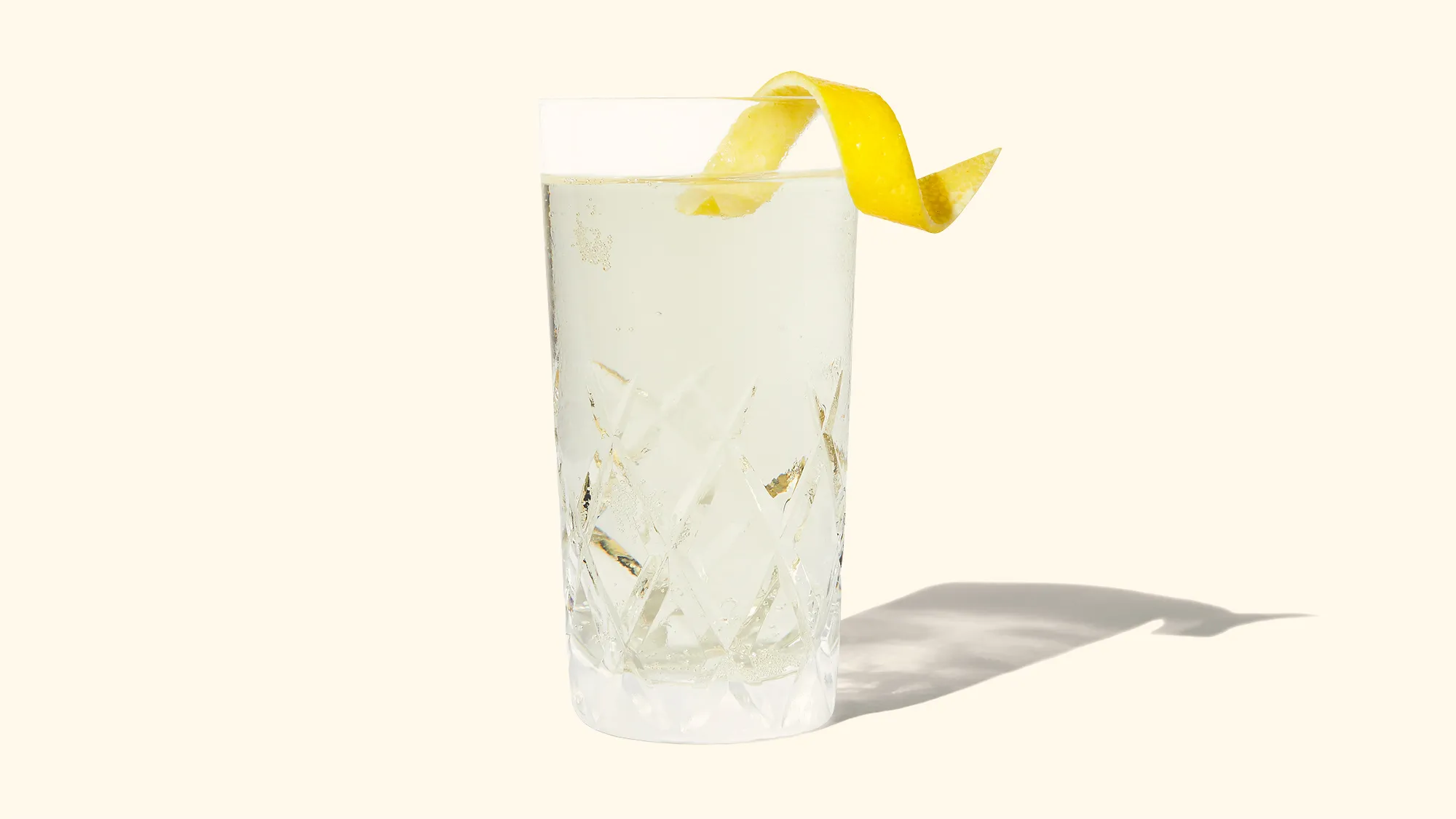 A tall whiskey highball with clear ice, bubbly soda, and a lemon twist on a neutral kitchen counter with soft natural light