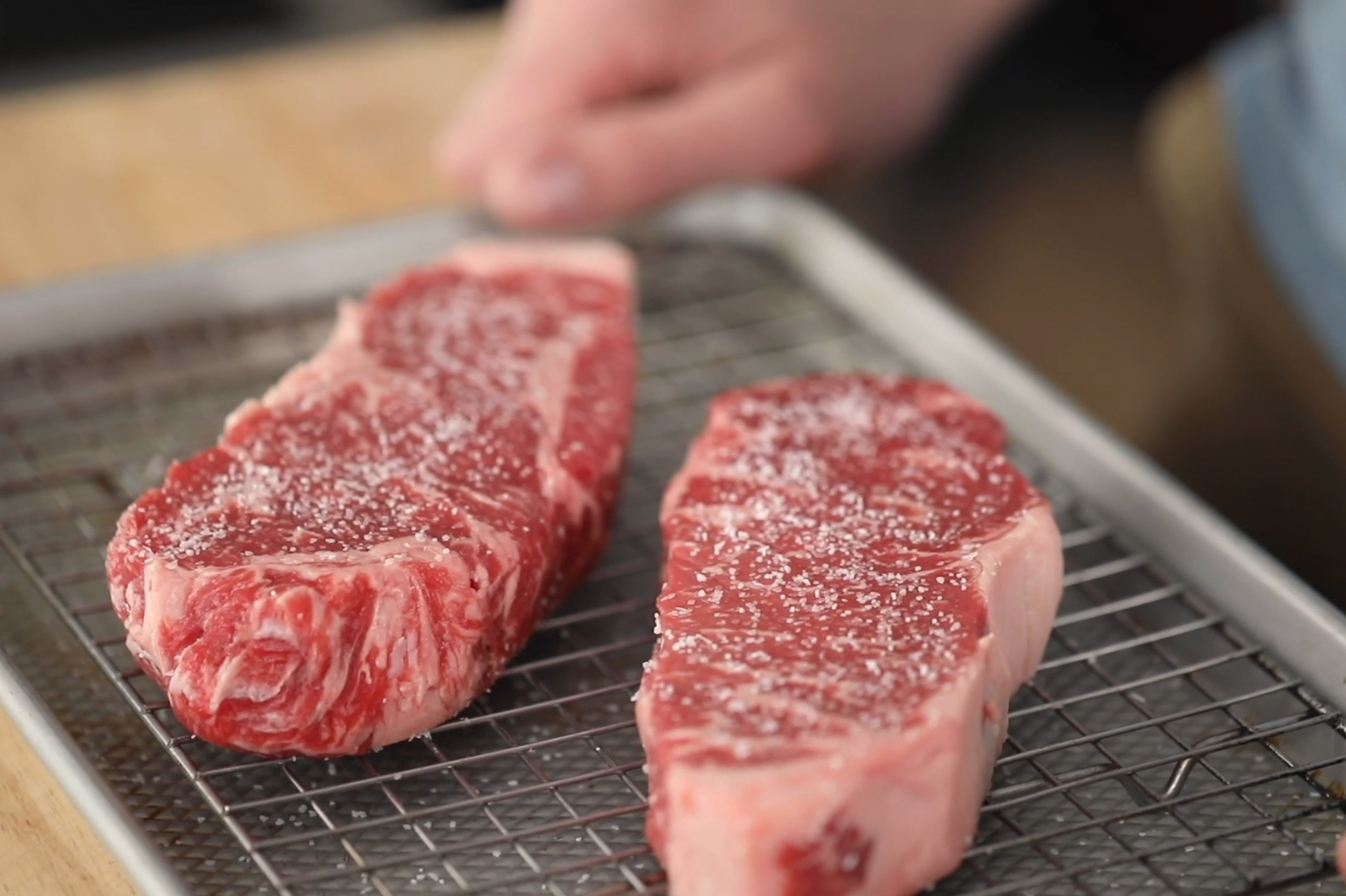 A thick ribeye steak with a deep brown crust searing in a cast iron skillet on a stovetop under warm kitchen lighting