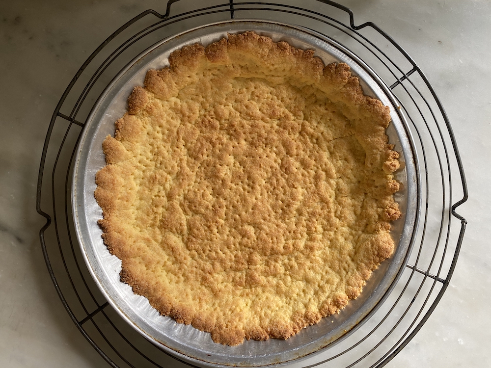 A thick yellow cake mix batter being pressed evenly into the bottom of a parchment-lined baking dish on a kitchen counter
