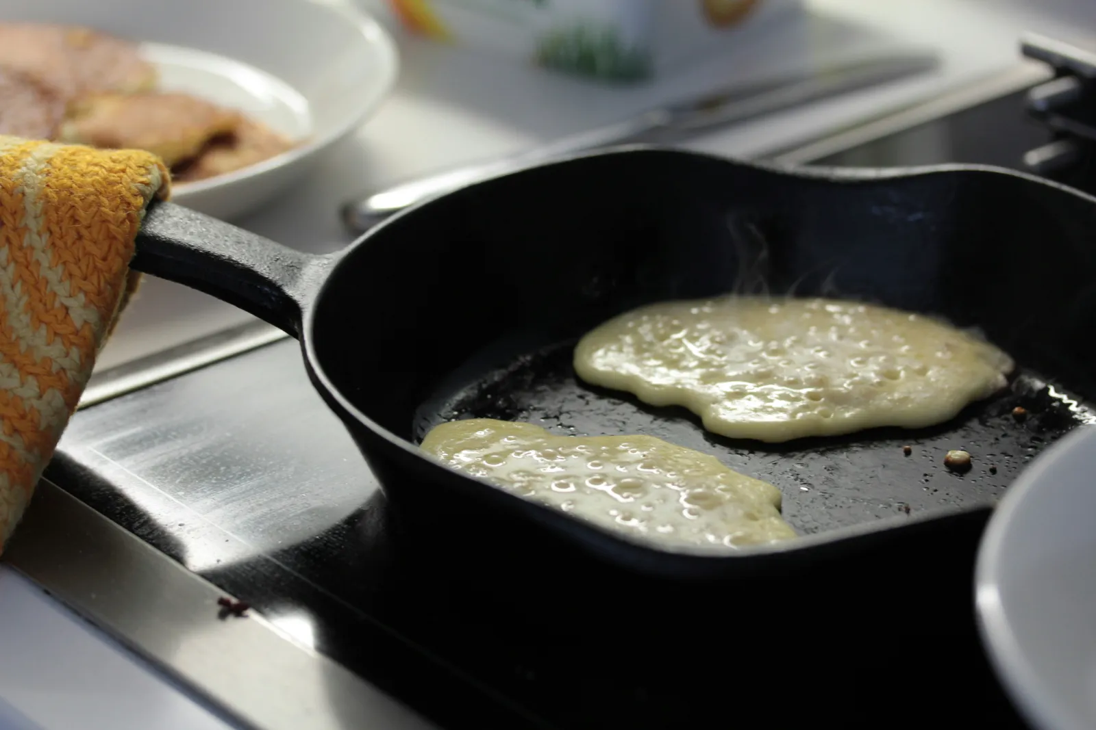 A thin pancake being lifted with a spatula and flipped in a nonstick skillet on a stovetop, with butter bubbling lightly
