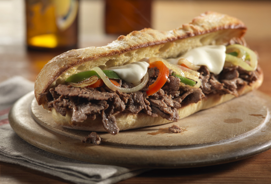 A toasted hoagie roll filled with crisp-edged shaved beef, sweet browned onions, and melted provolone on a wooden board