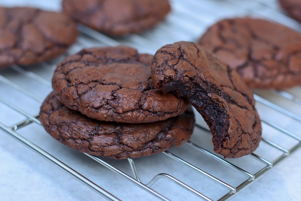 A tray of brownie mix cookies with shiny crackly tops cooling on a wire rack on a warm-lit kitchen counter