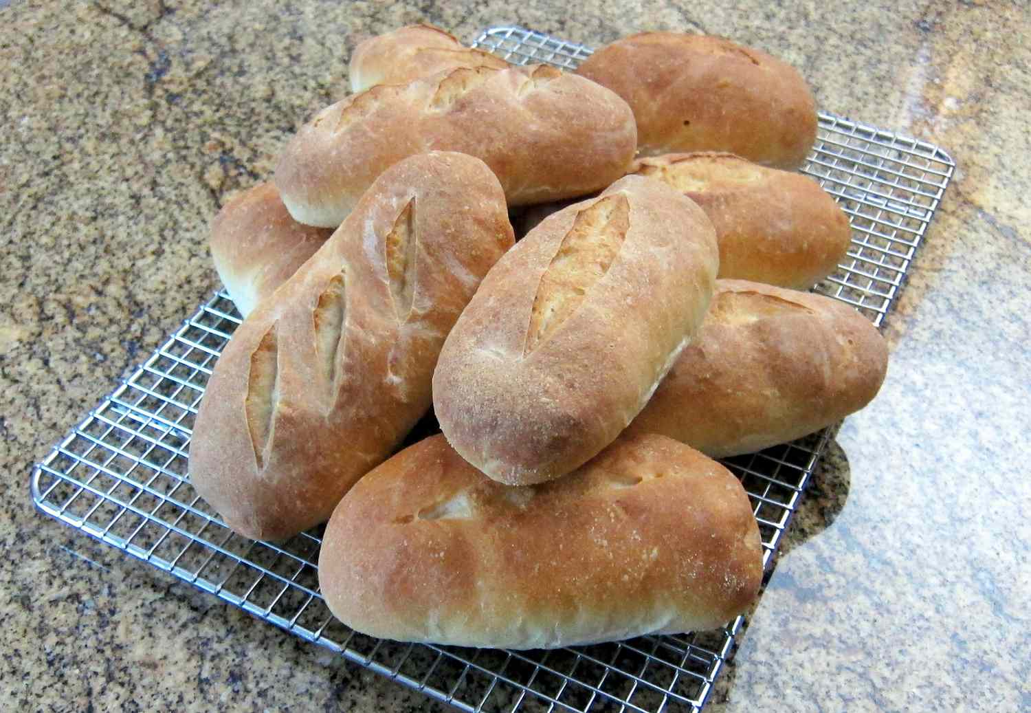 A tray of freshly baked hoagie rolls on parchment paper with golden tops and a small bowl of melted butter on a warm kitchen counter