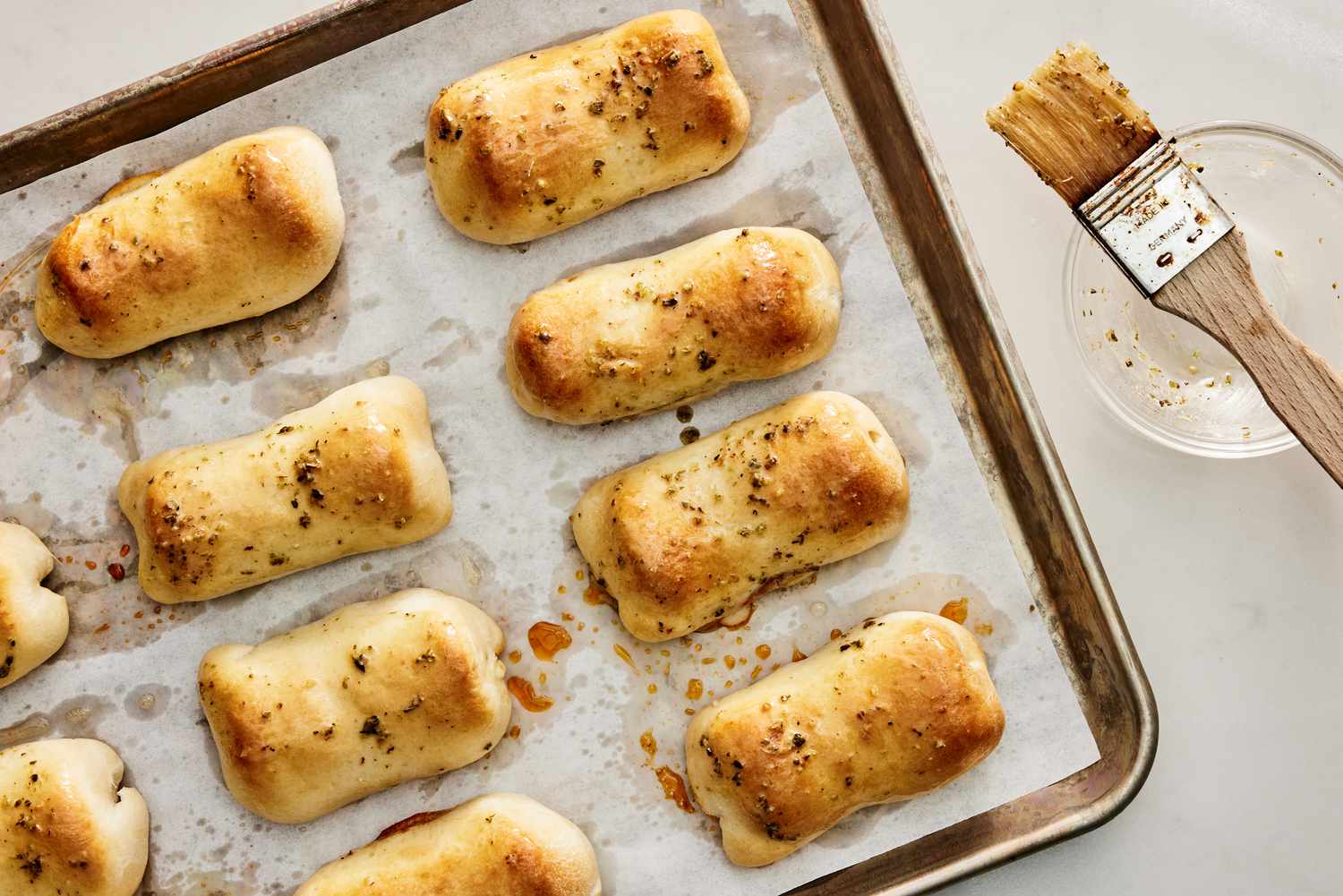 A tray of golden baked pepperoni rolls on a parchment lined sheet pan, some cut open to show melted mozzarella and pepperoni spirals, warm kitchen lighting